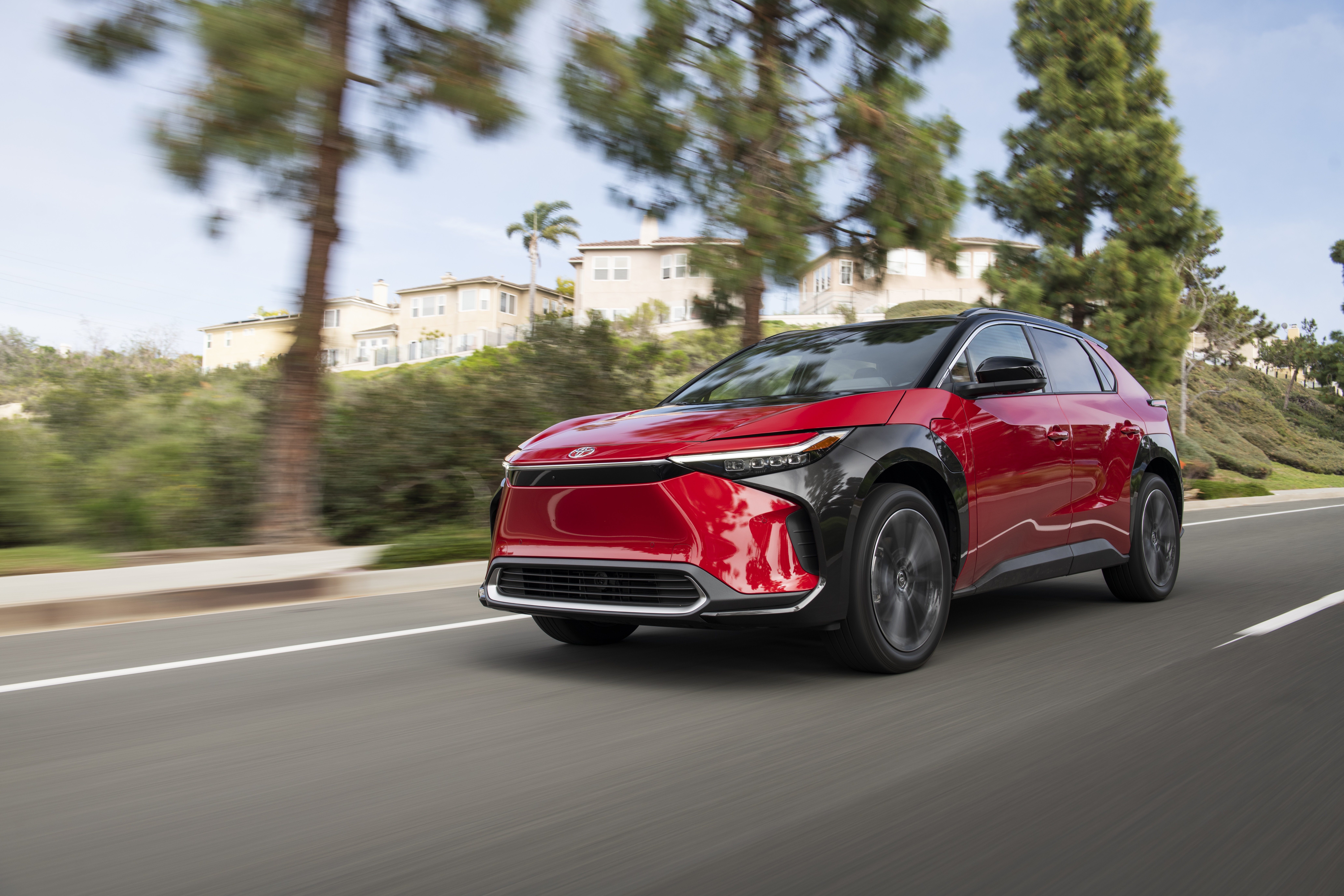 Red Toyota BZ4X driving on a suburban road HD Wallpaper