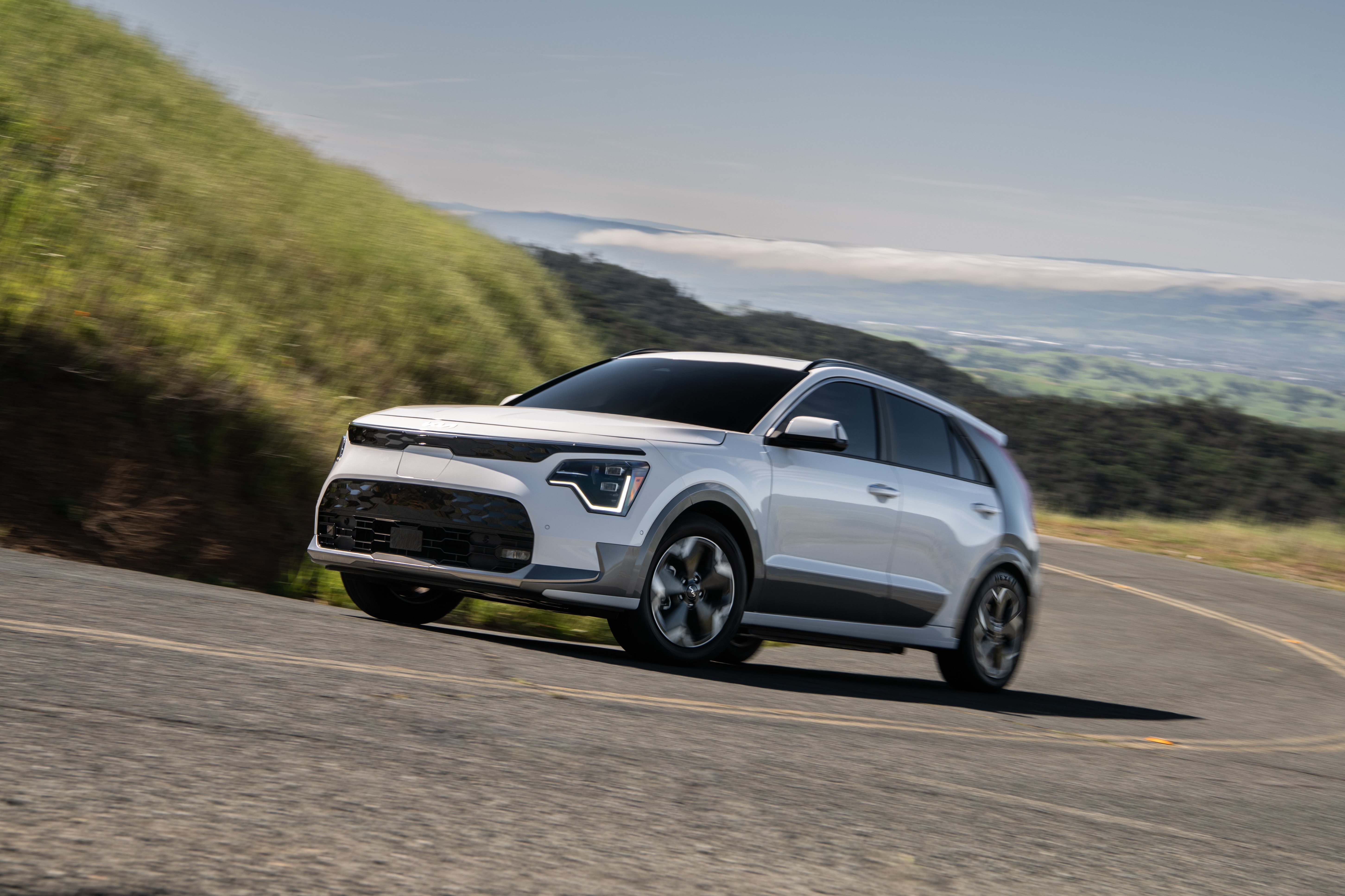 White Kia Niro driving on a winding road HD Wallpaper
