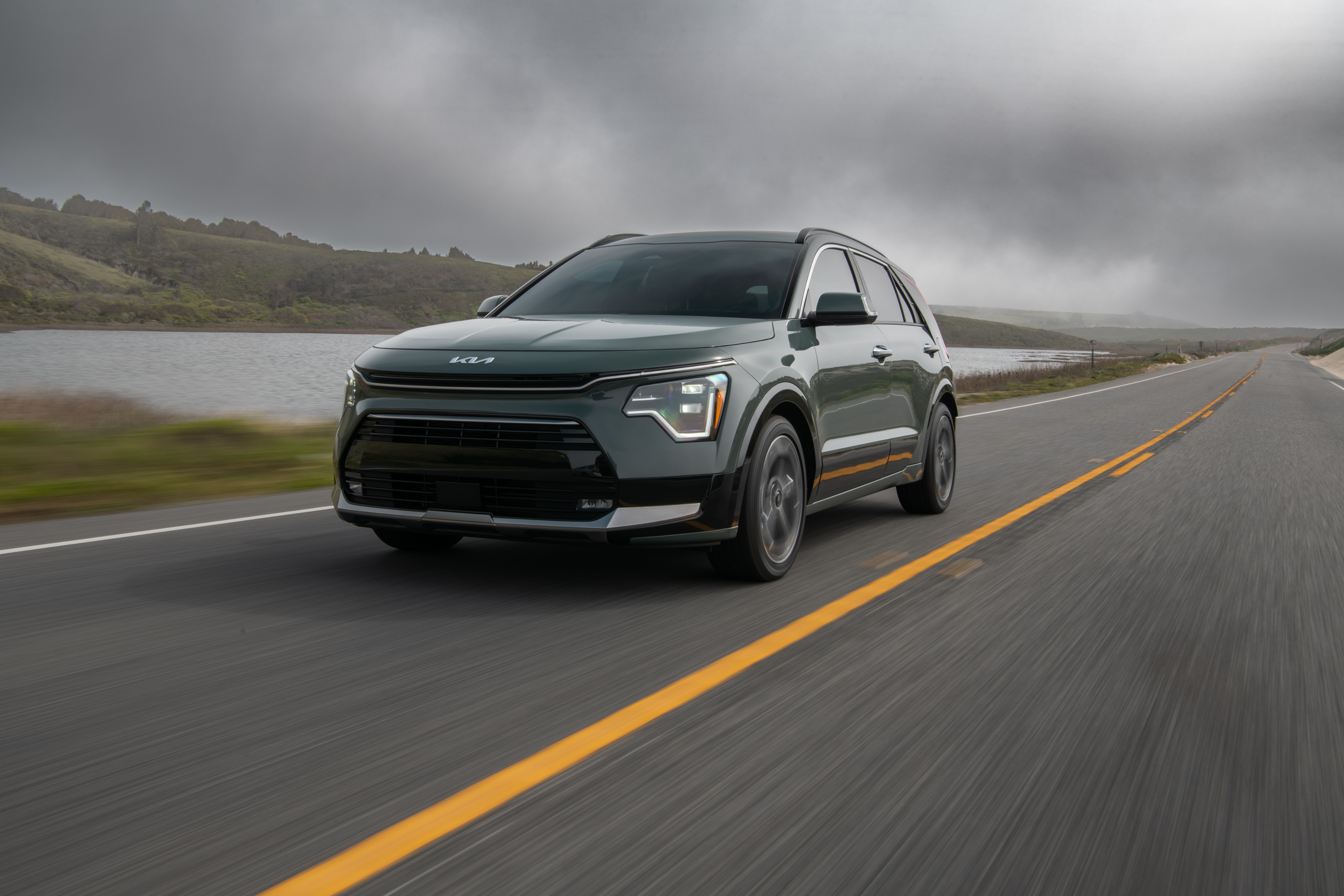 Kia Niro driving on a coastal road HD Wallpaper