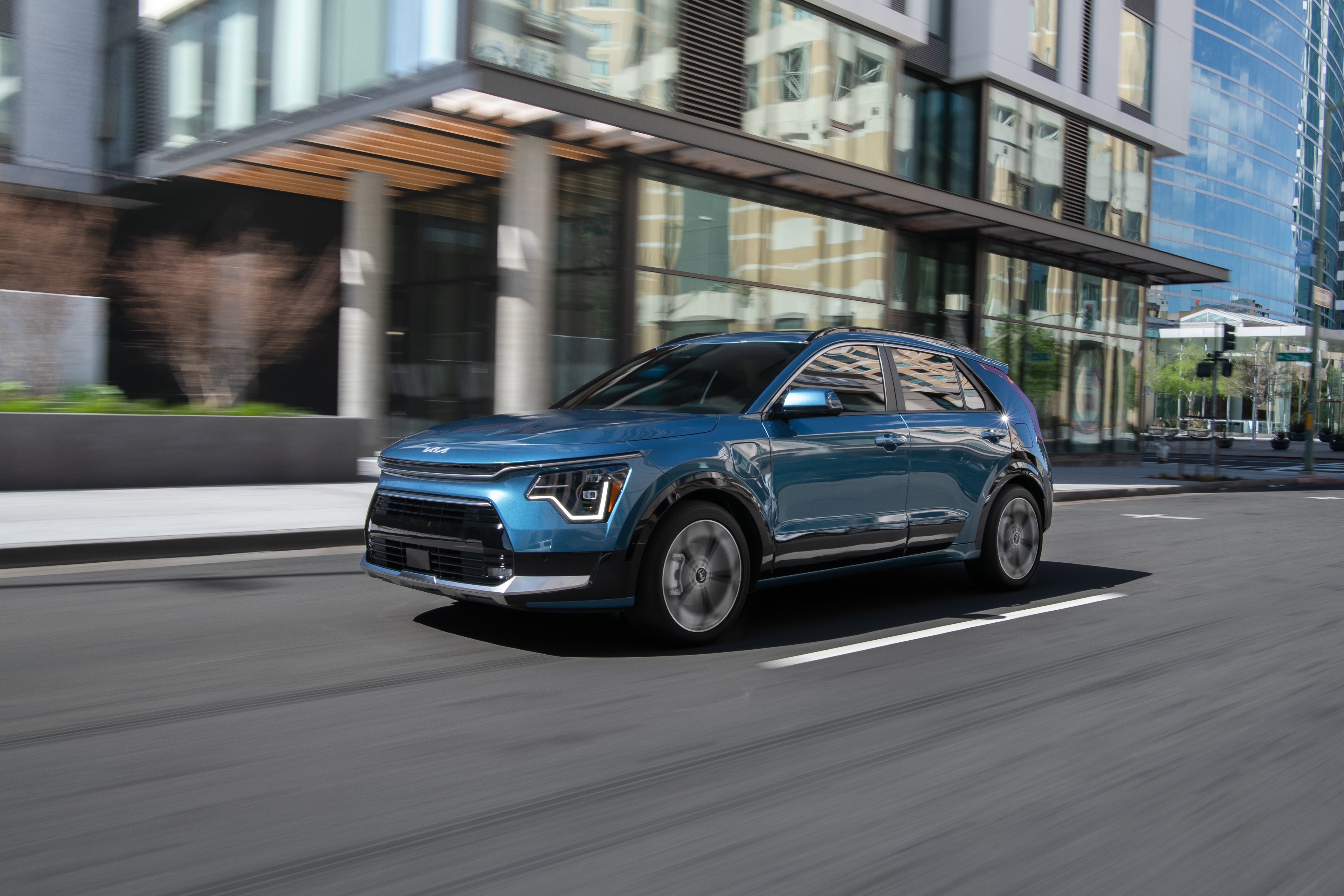 Blue Kia Niro driving on city street HD Wallpaper