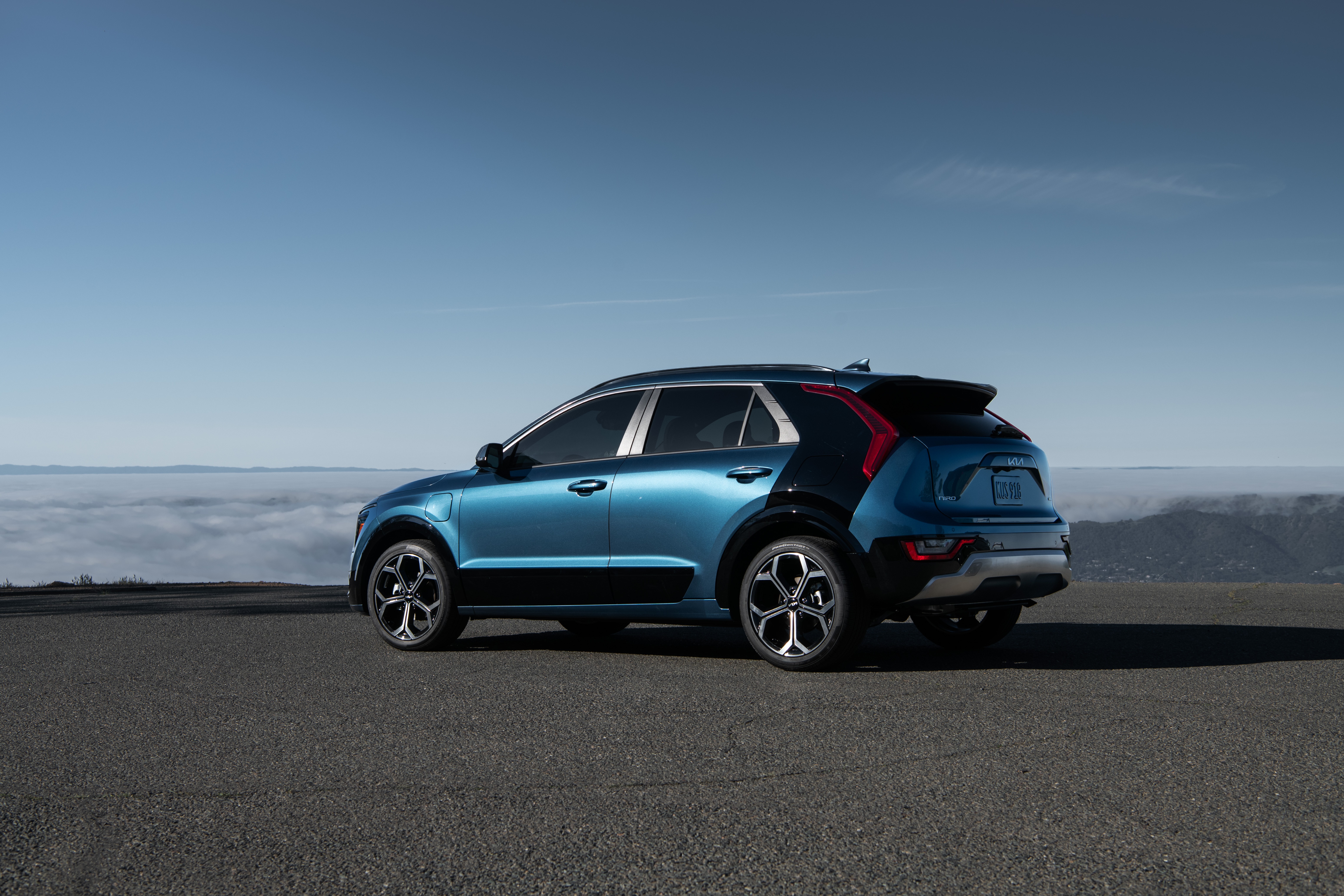 Blue Kia Niro parked on a road with clouds below HD Wallpaper