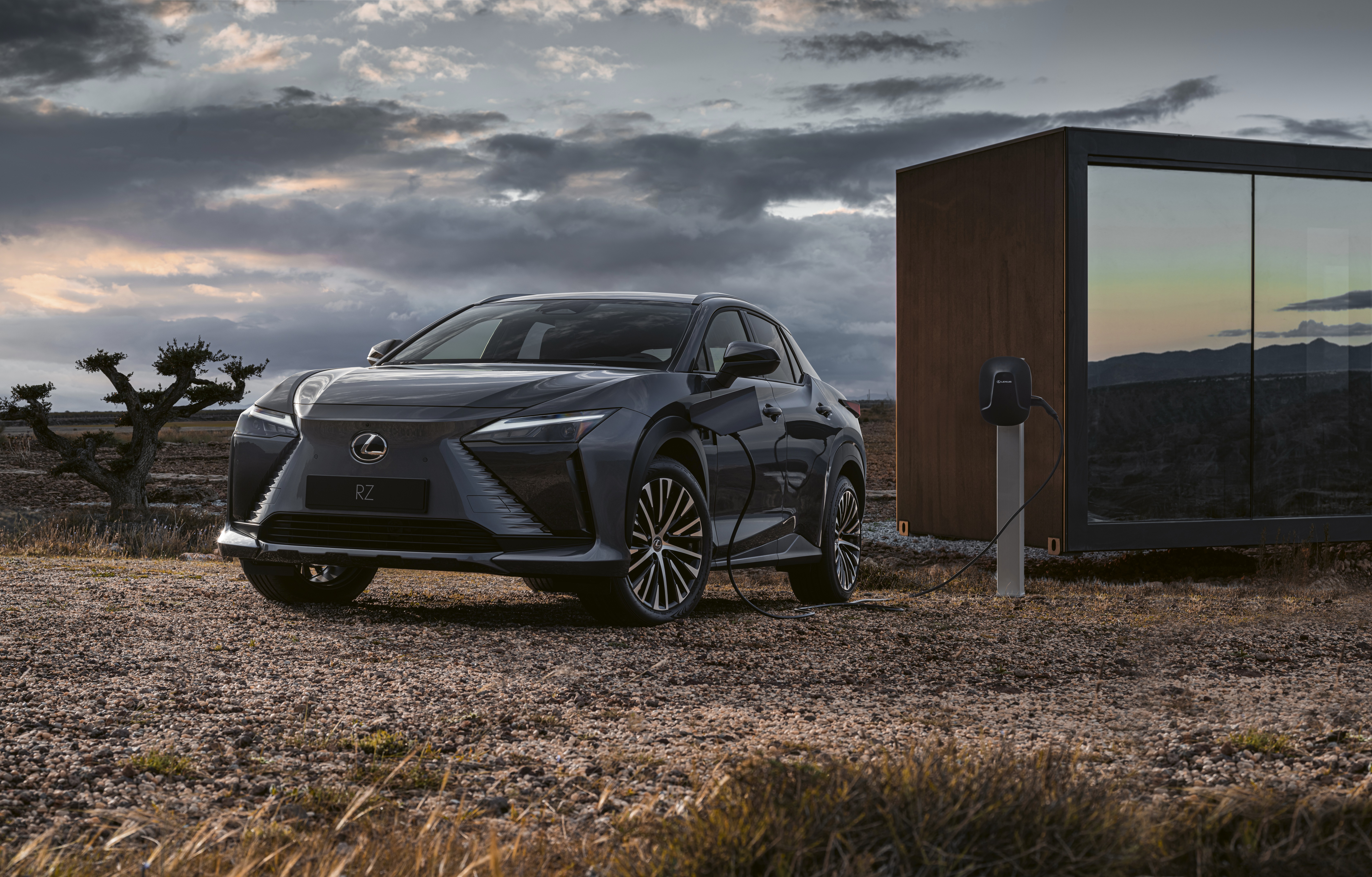 Lexus RZ 450e charging next to a modern cabin HD Wallpaper
