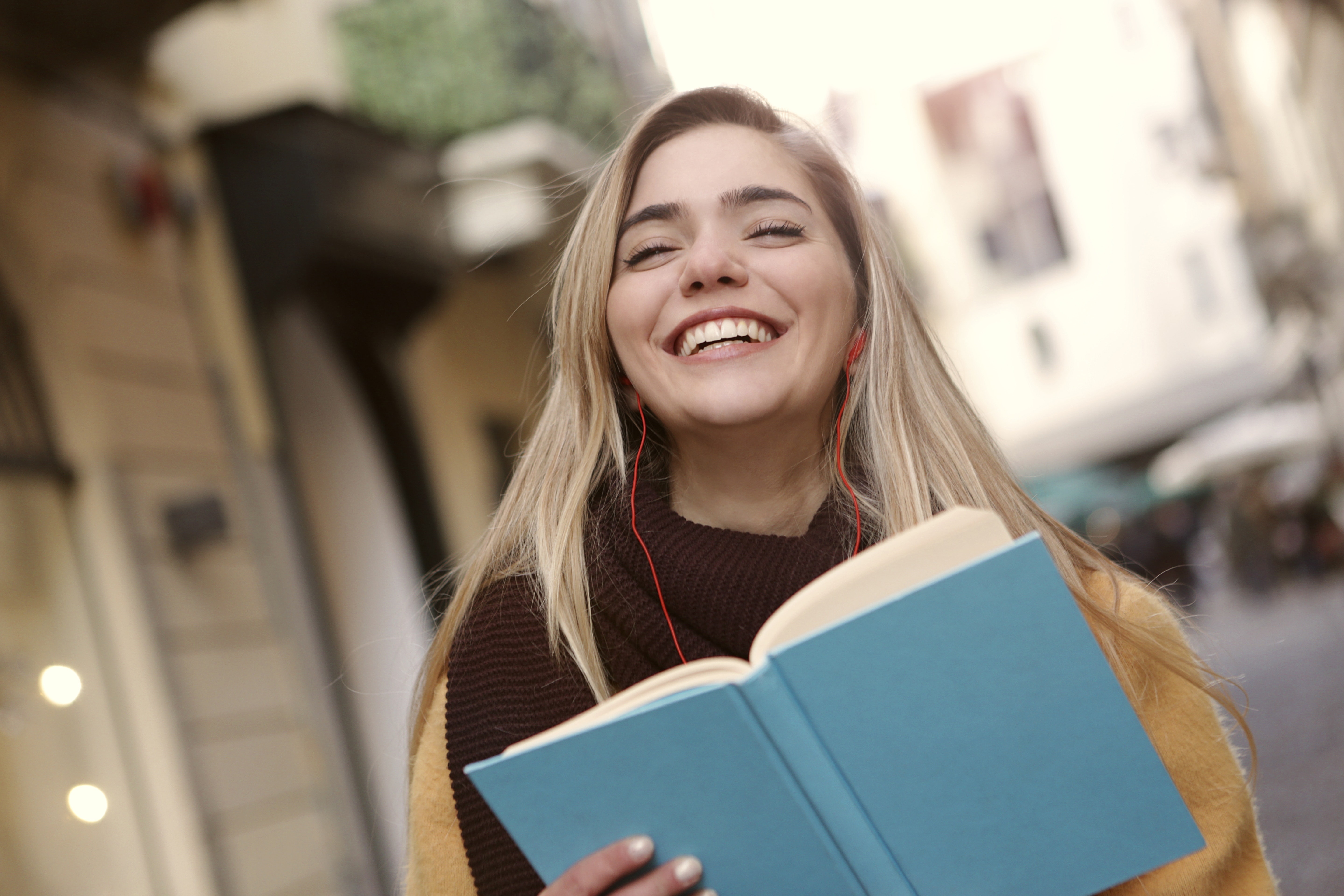 Young woman laughing while reading a book outdoors HD Wallpaper