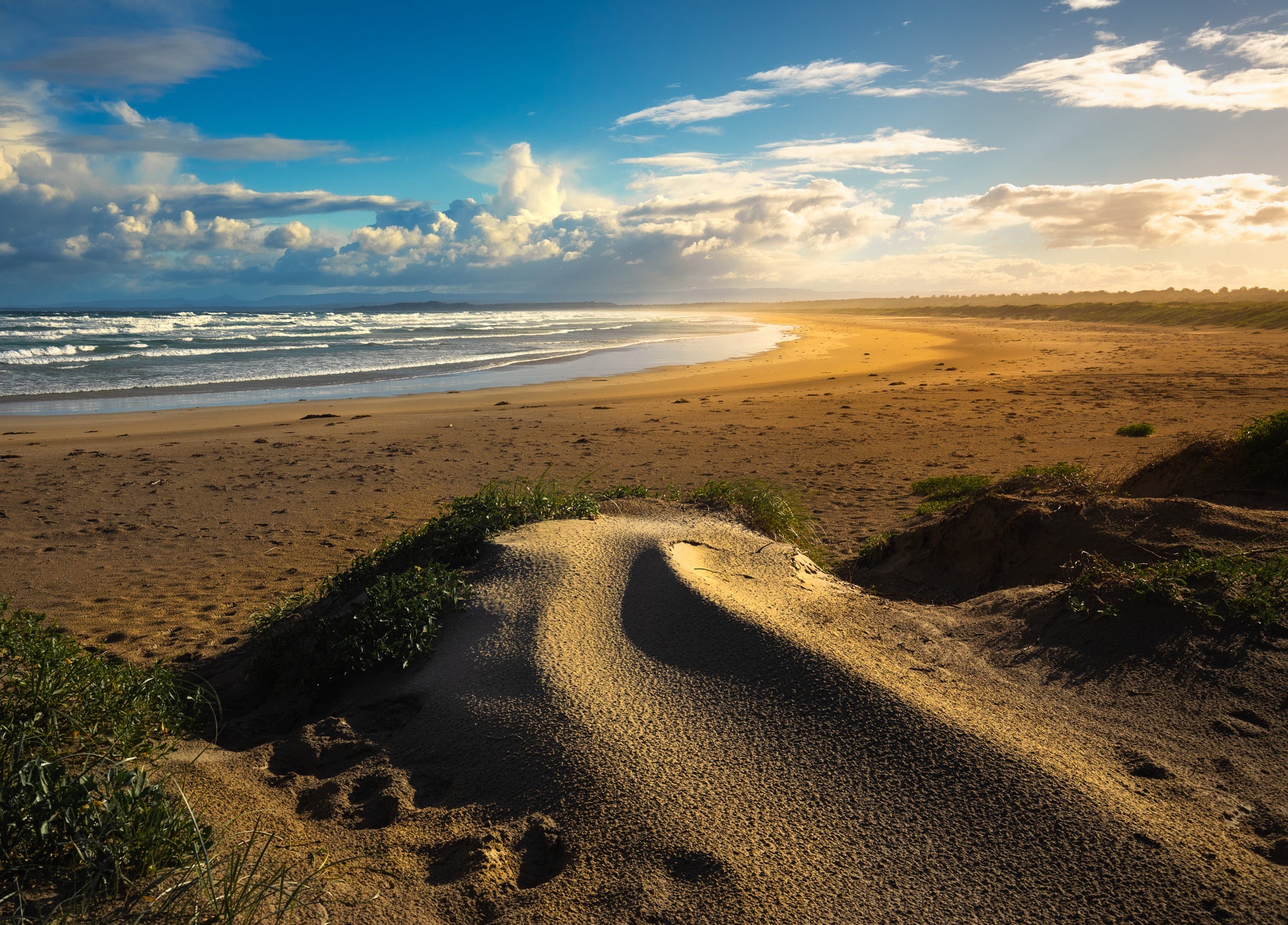 Sandy beach with ocean waves and clouds at sunset HD Wallpaper
