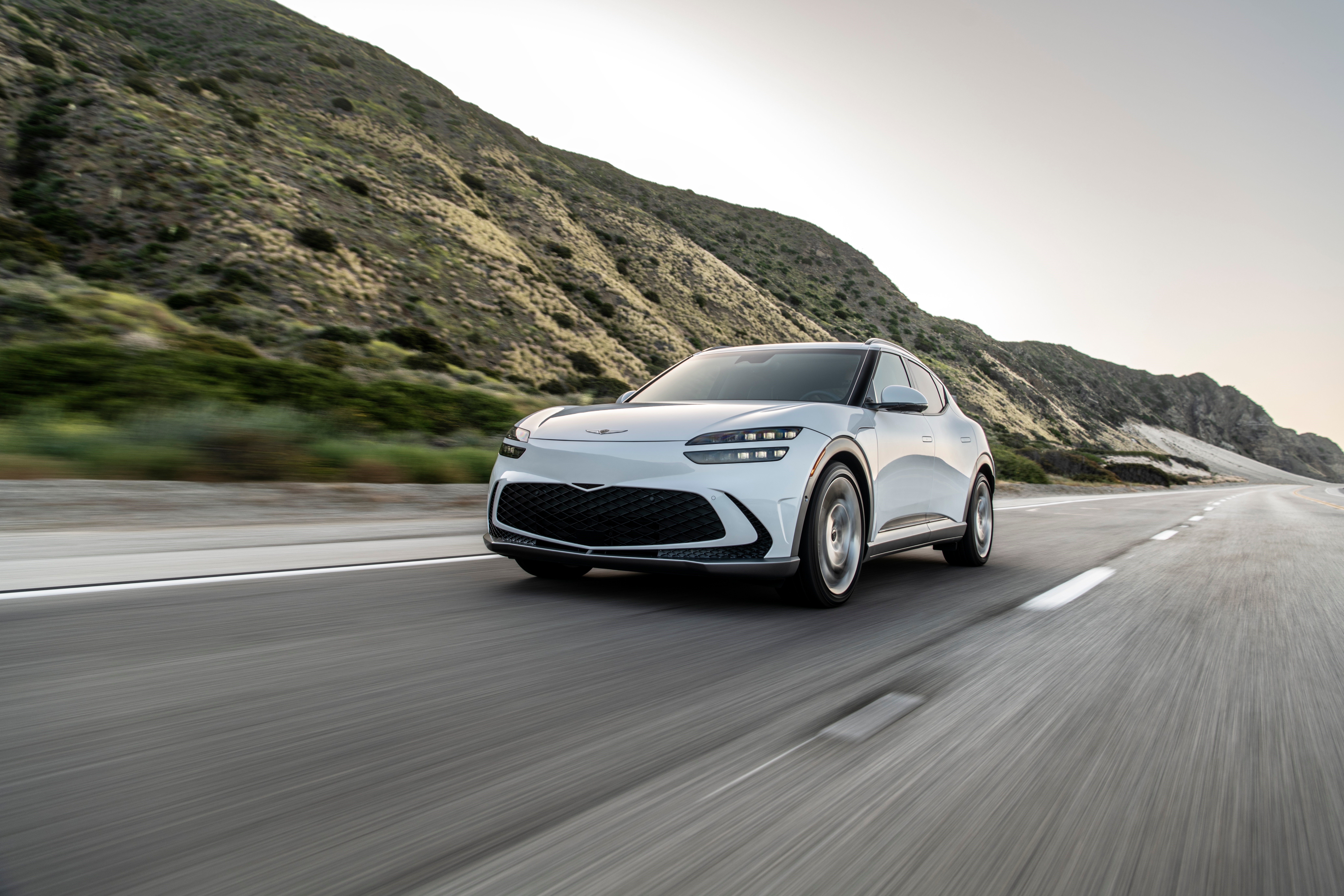 White Genesis GV60 driving on a coastal road HD Wallpaper