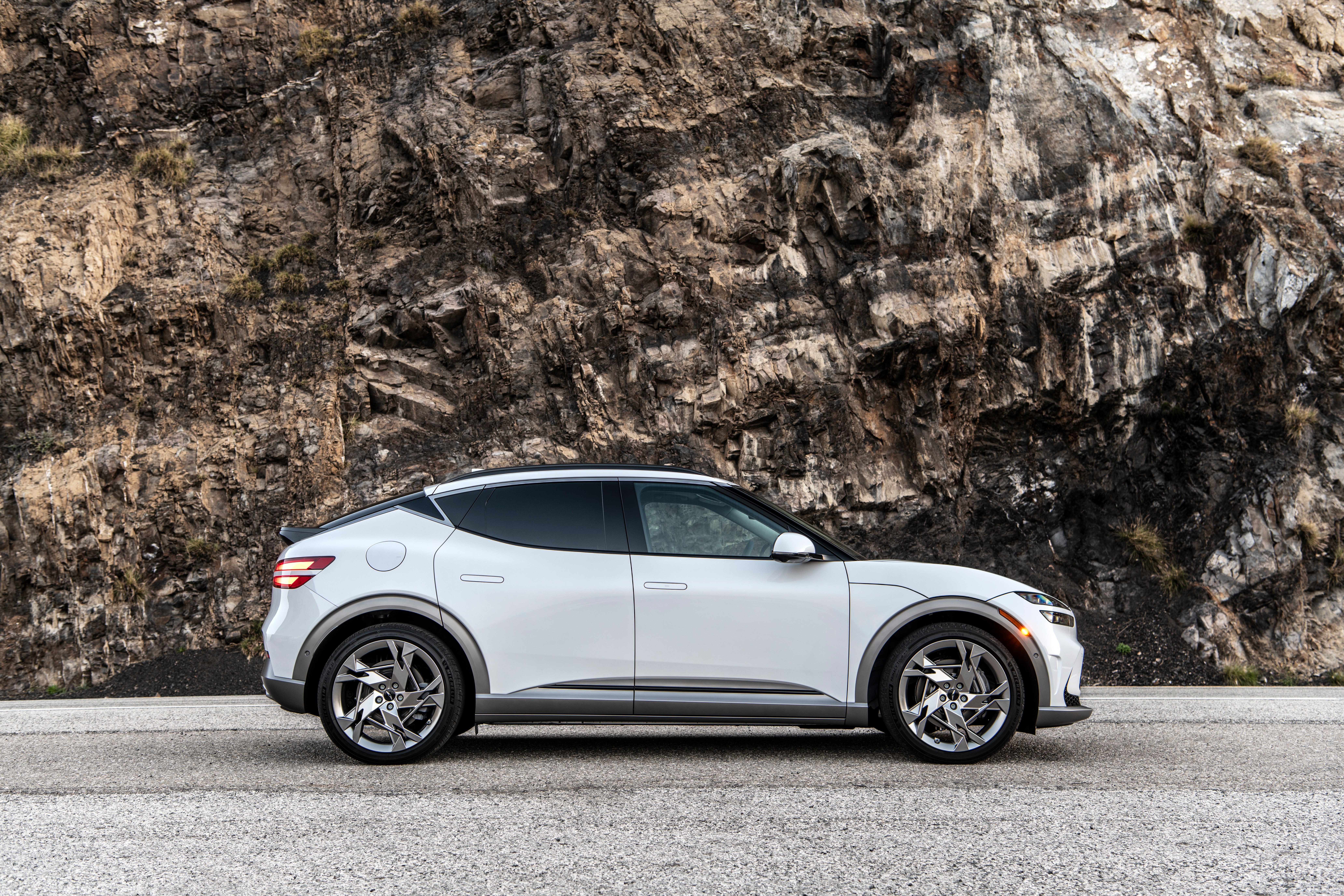 White Genesis GV60 parked on a road with rocky mountain background HD Wallpaper