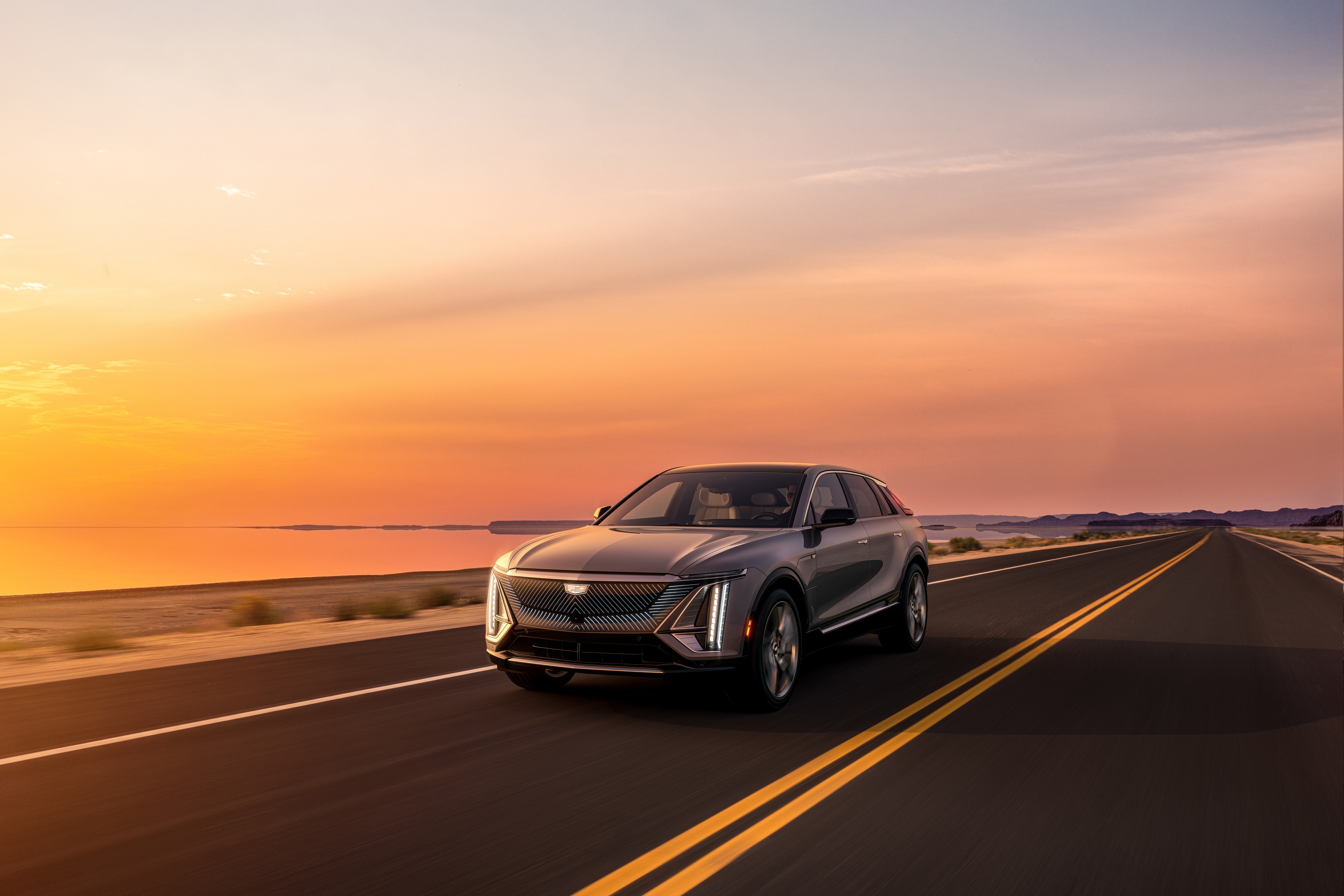 Cadillac Lyriq driving on a road at sunset HD Wallpaper
