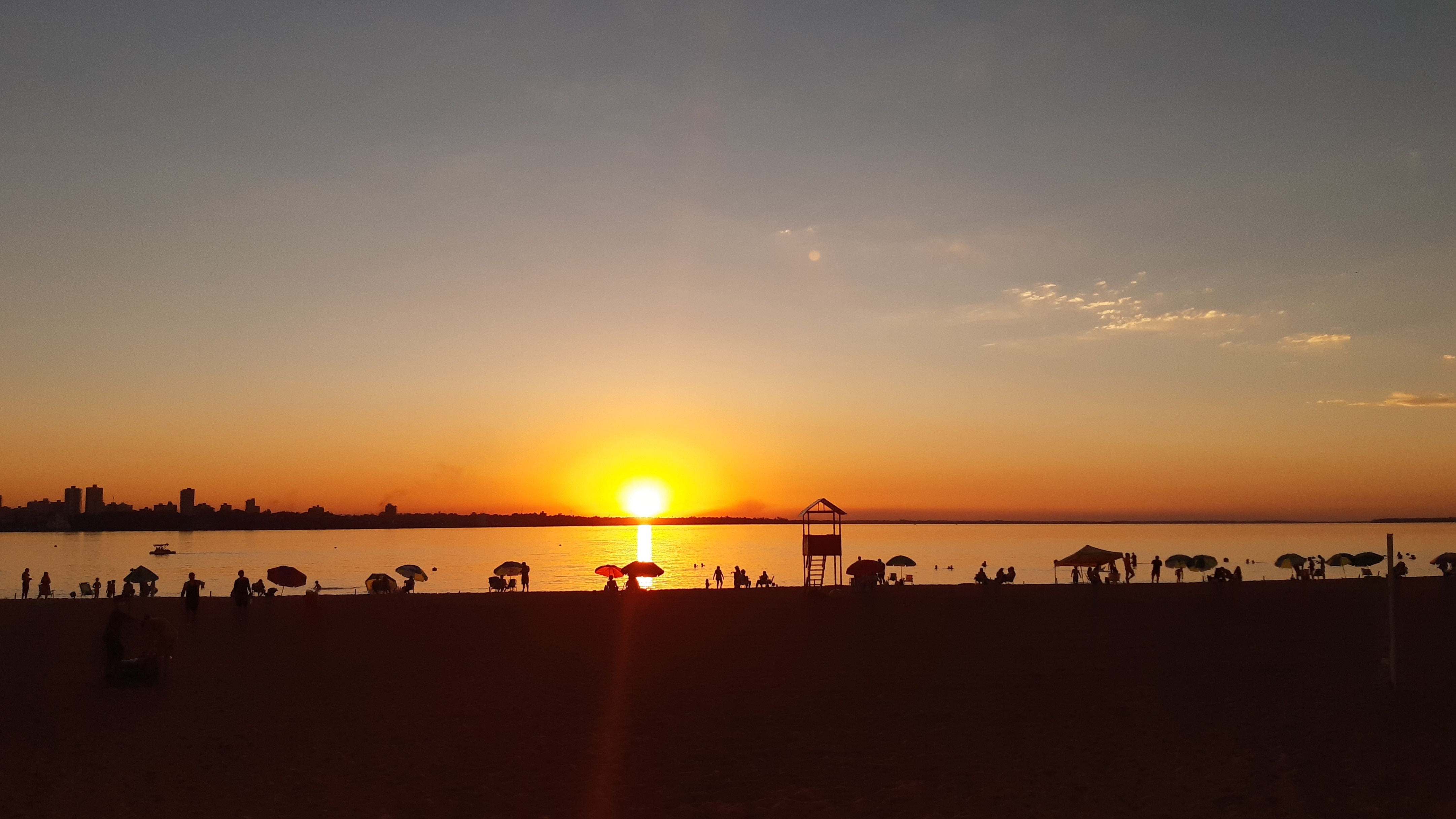 Sunset over a beach with people and a city skyline HD Wallpaper