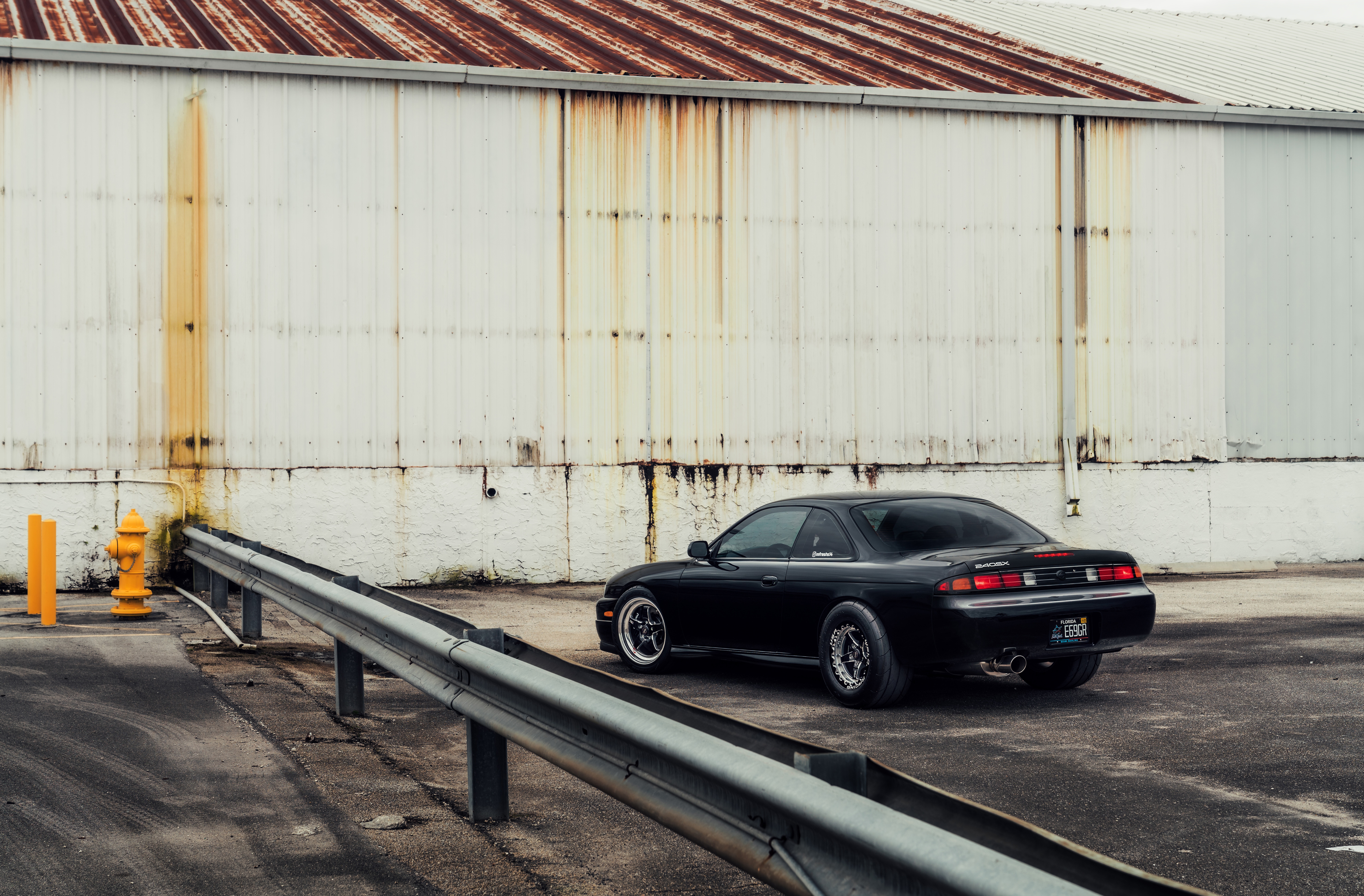 Black Nissan 240SX parked near a warehouse HD Wallpaper