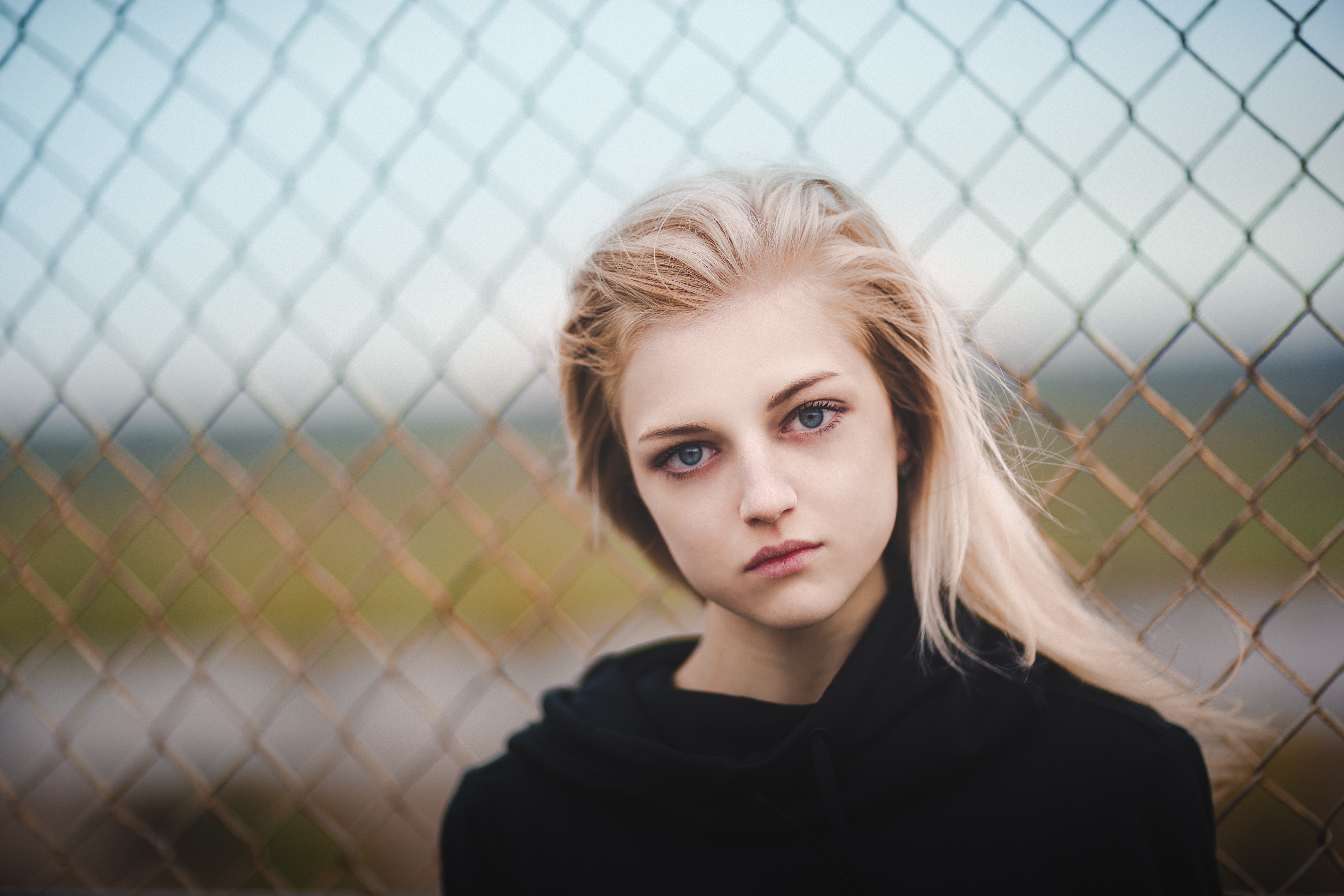 Blonde girl in black hoodie behind fence HD Wallpaper