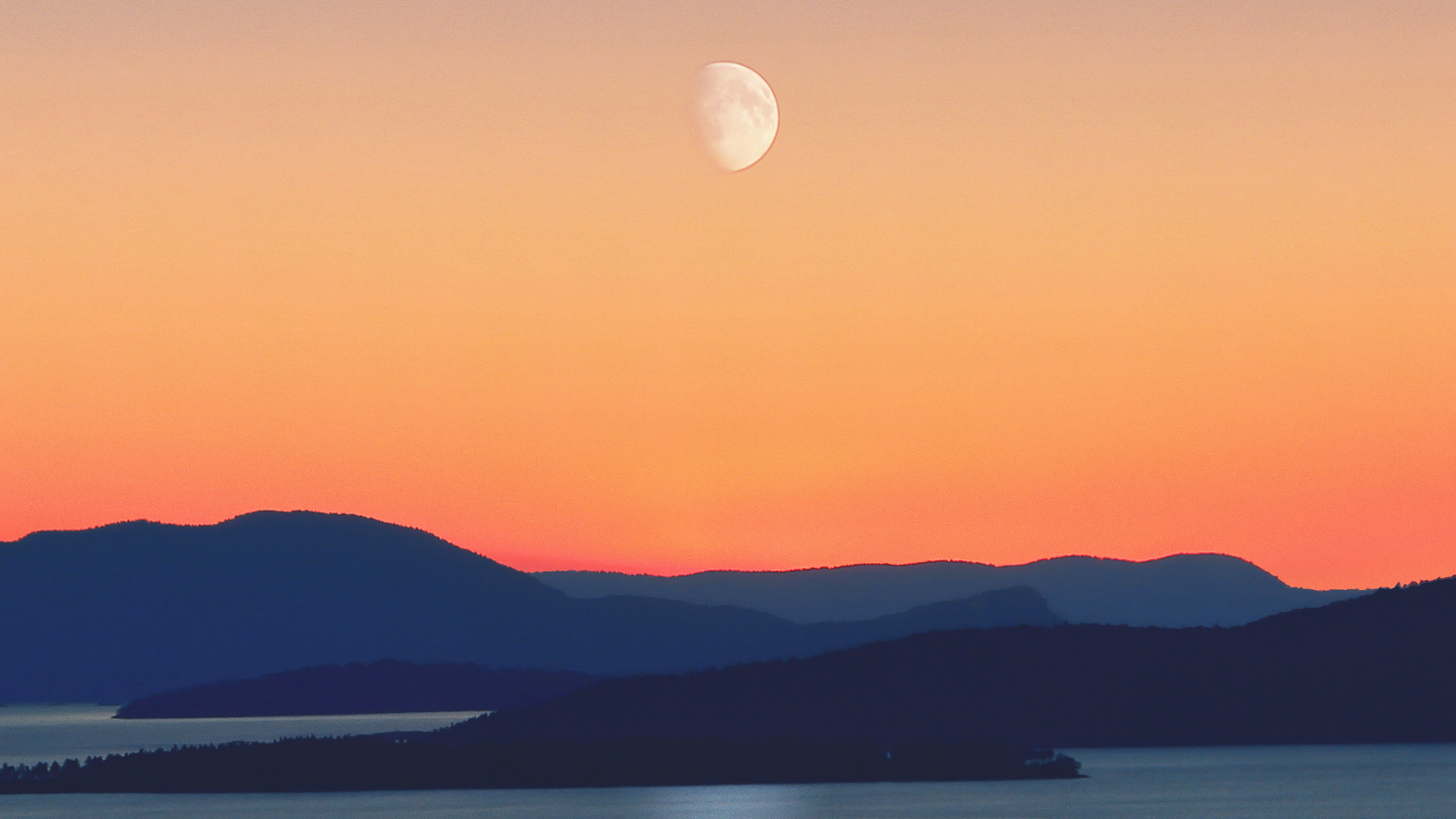 Moon over silhouetted mountains and water at sunset HD Wallpaper