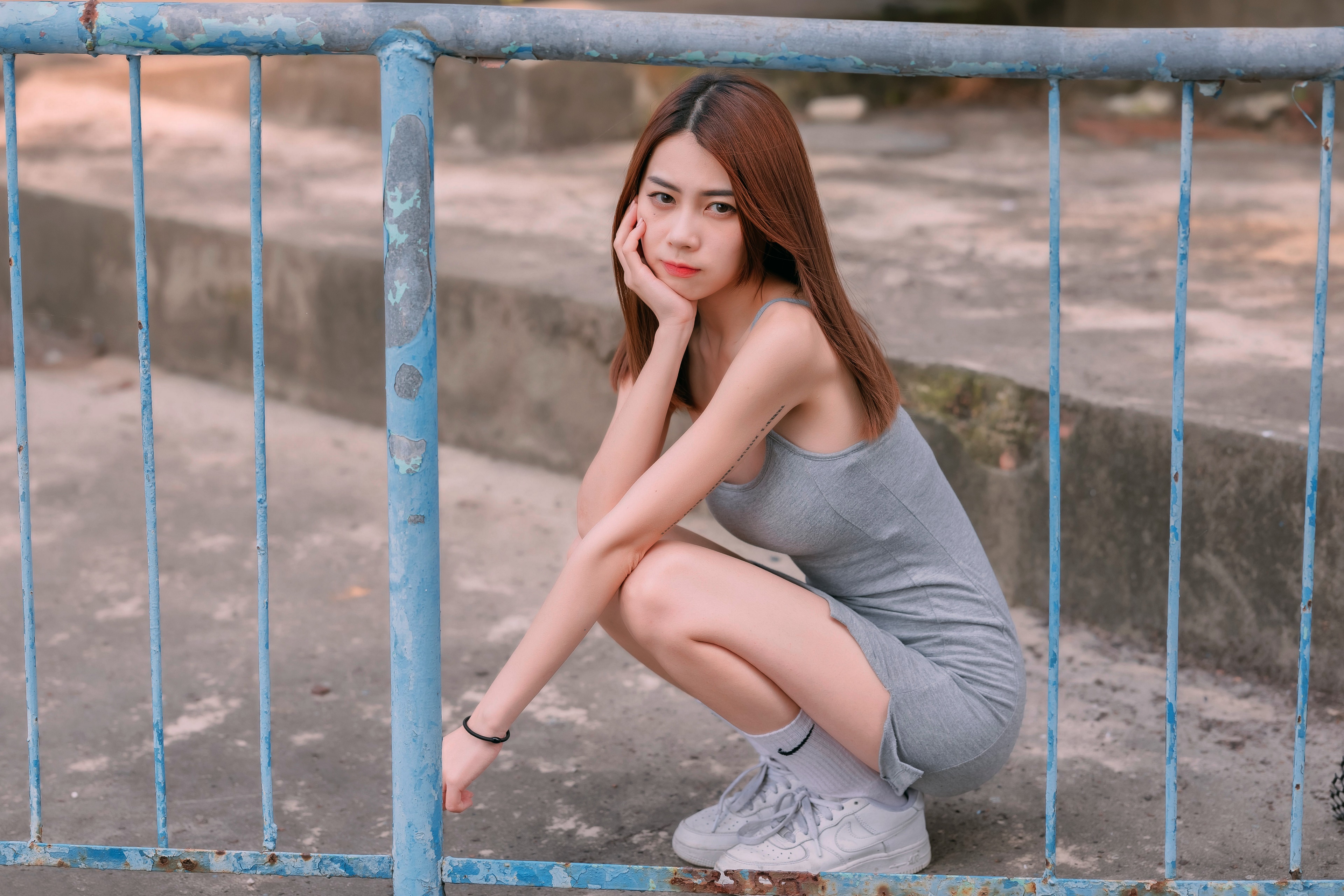Asian woman in grey dress squatting by a fence HD Wallpaper