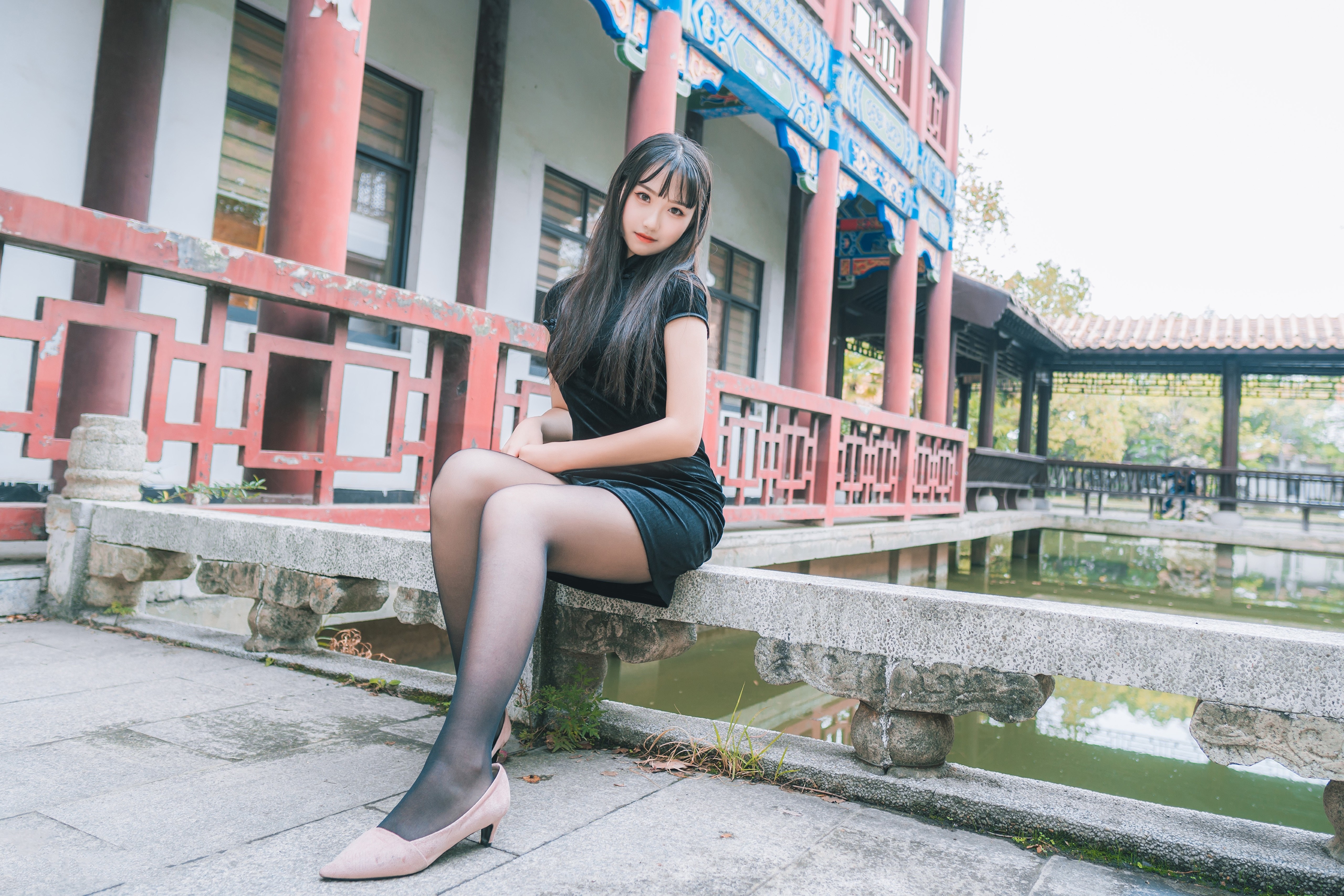 Brunette girl in black dress sitting by pond HD Wallpaper