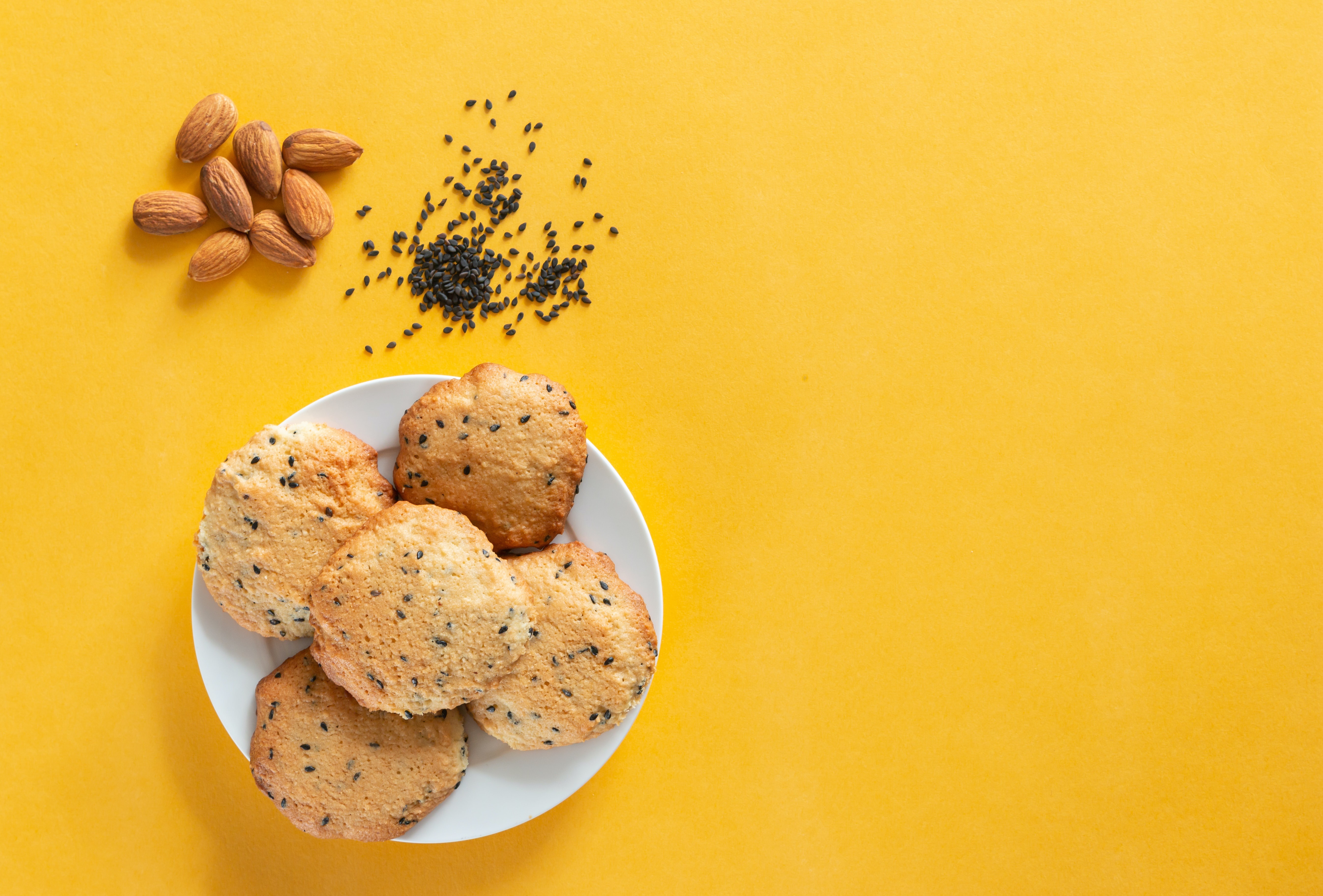 Cookies with almonds and sesame seeds on a yellow background HD Wallpaper