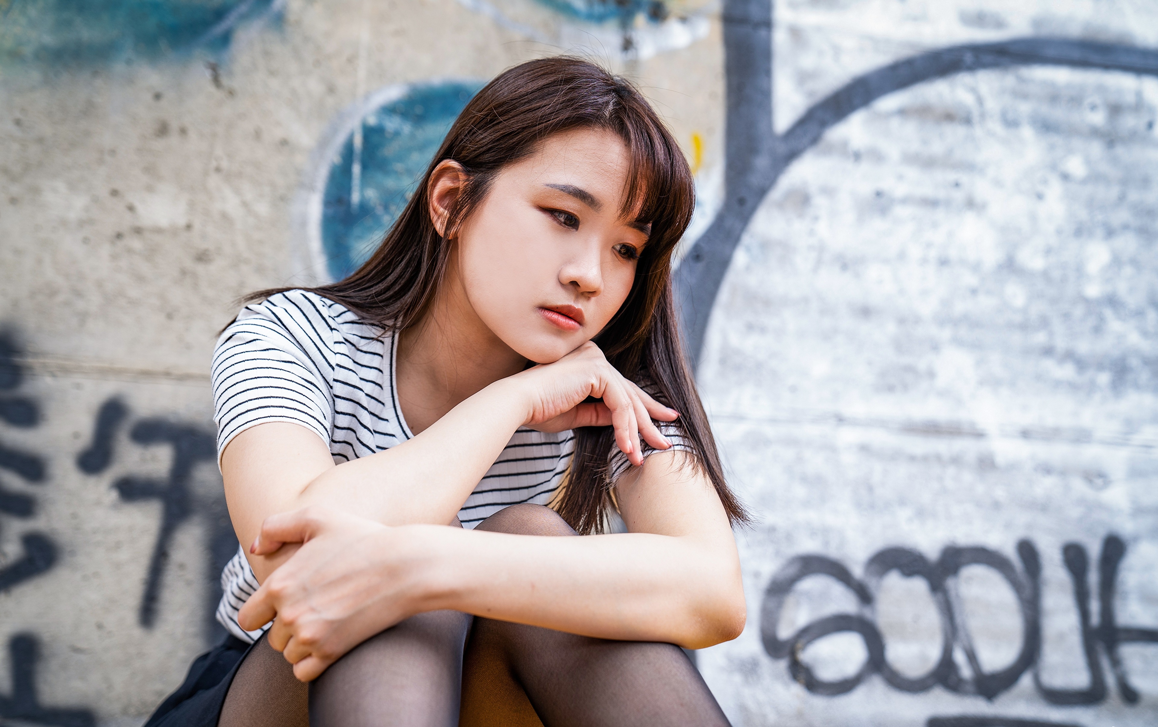 Sad Asian girl with brunette hair sitting by graffiti wall HD Wallpaper