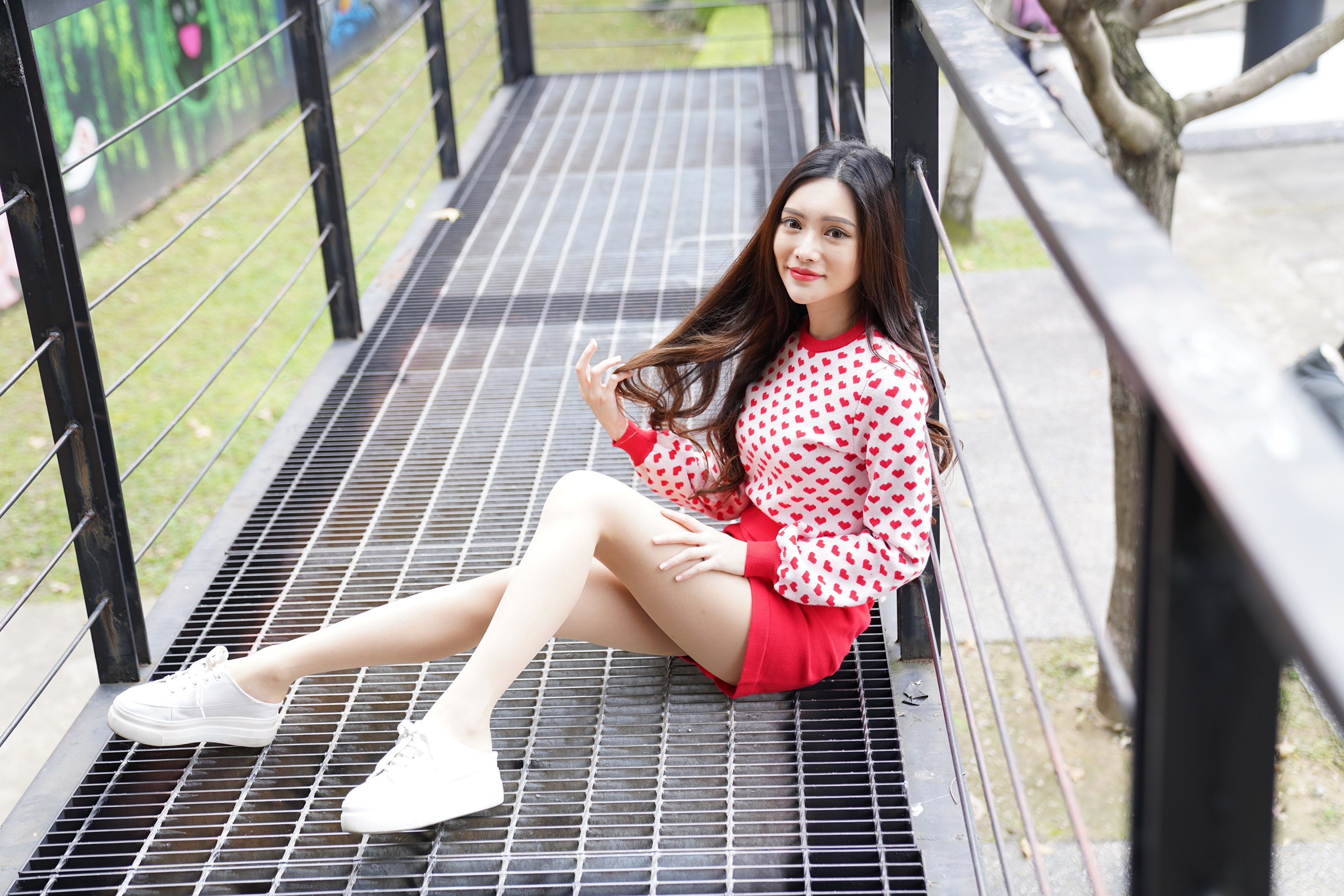 Asian woman in heart sweater sitting on metal walkway HD Wallpaper