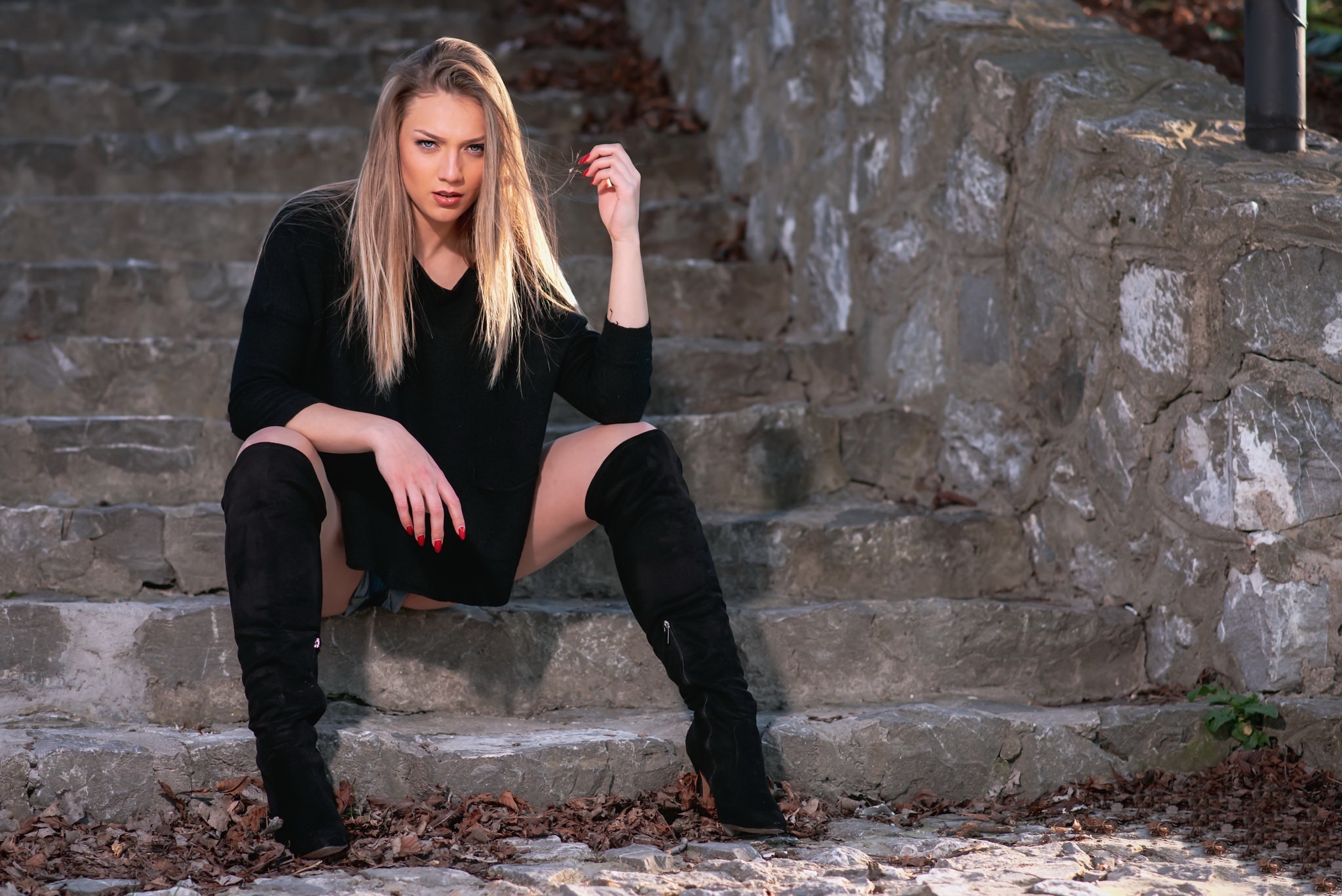Blonde woman sitting on stone stairs wearing black dress and boots HD Wallpaper
