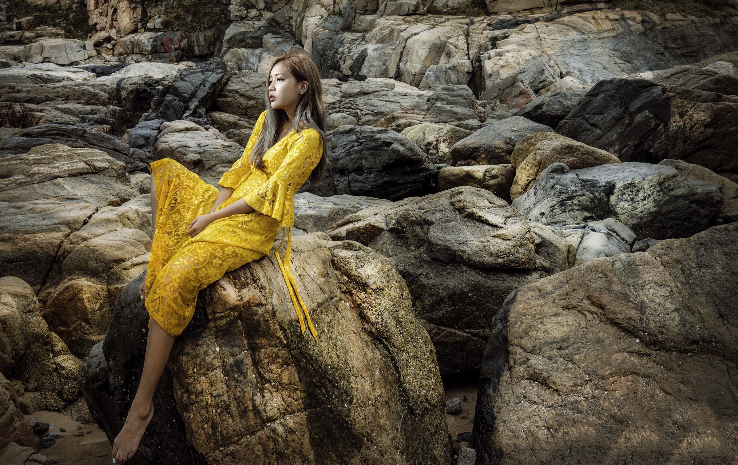 Woman in yellow dress sitting on rocks HD Wallpaper