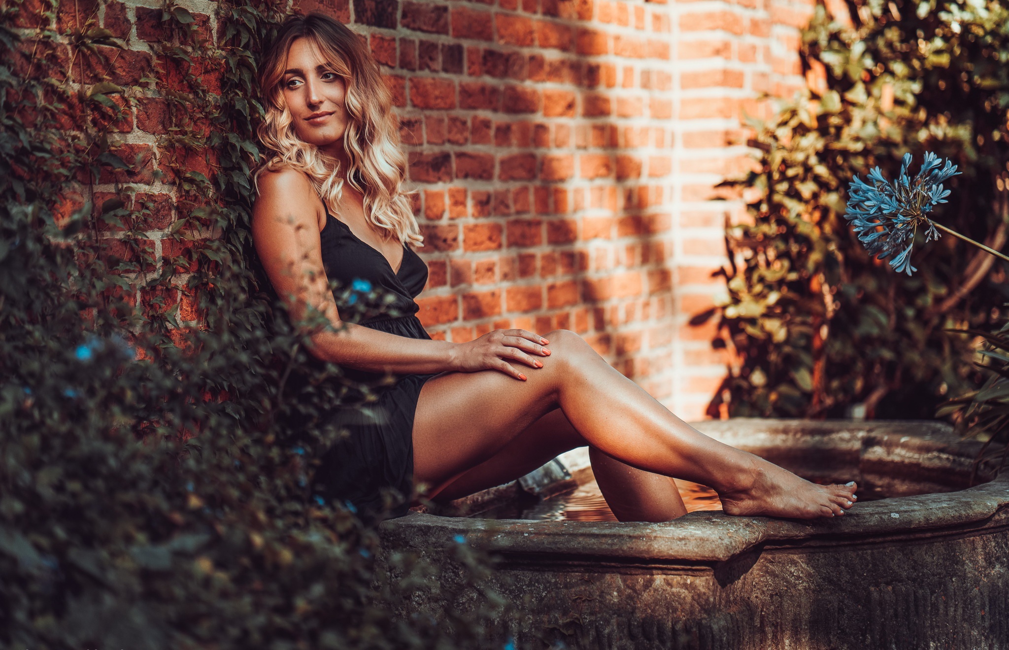 Woman in black dress sitting by brick wall HD Wallpaper