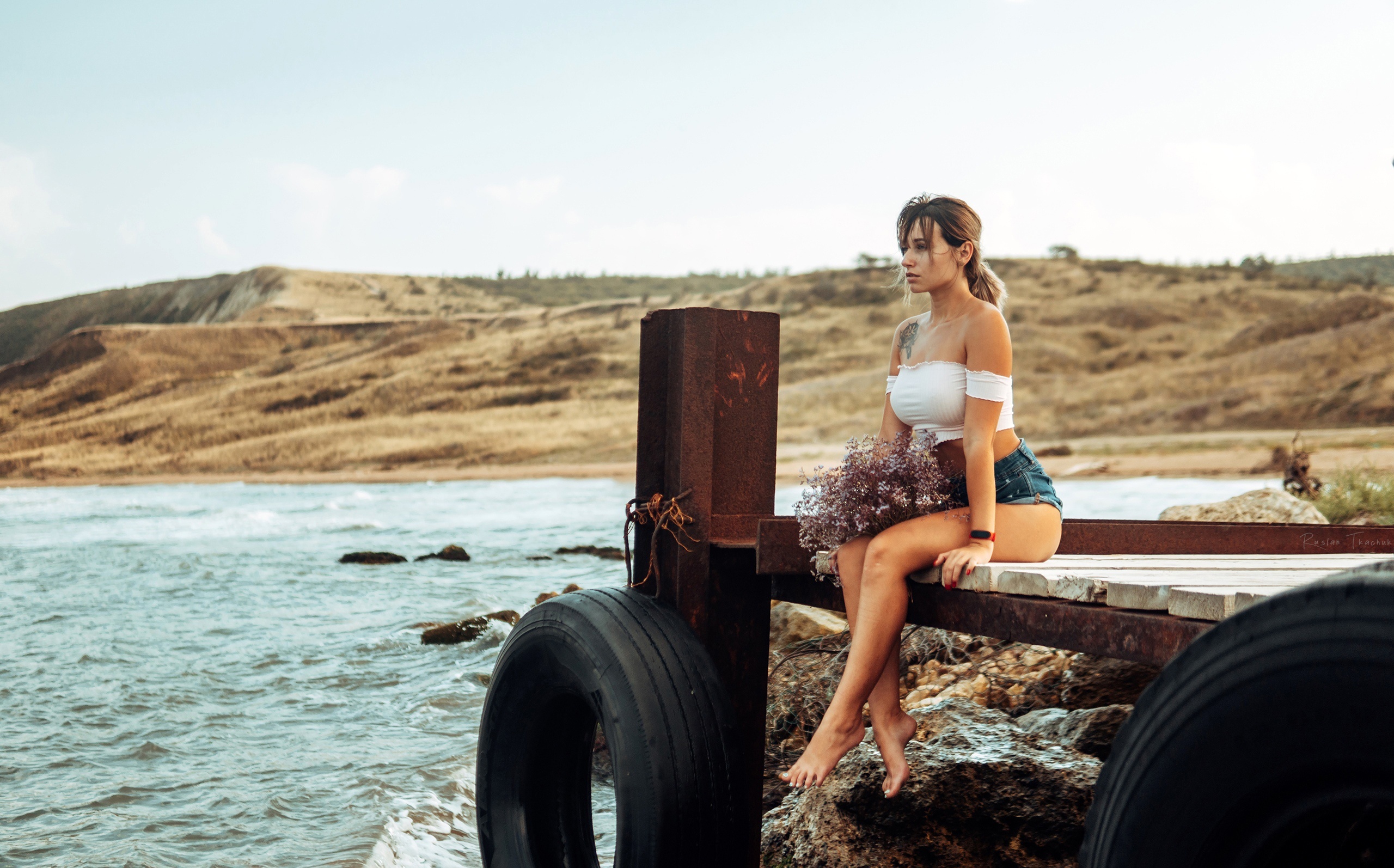 Woman in shorts sitting on a dock with flowers HD Wallpaper