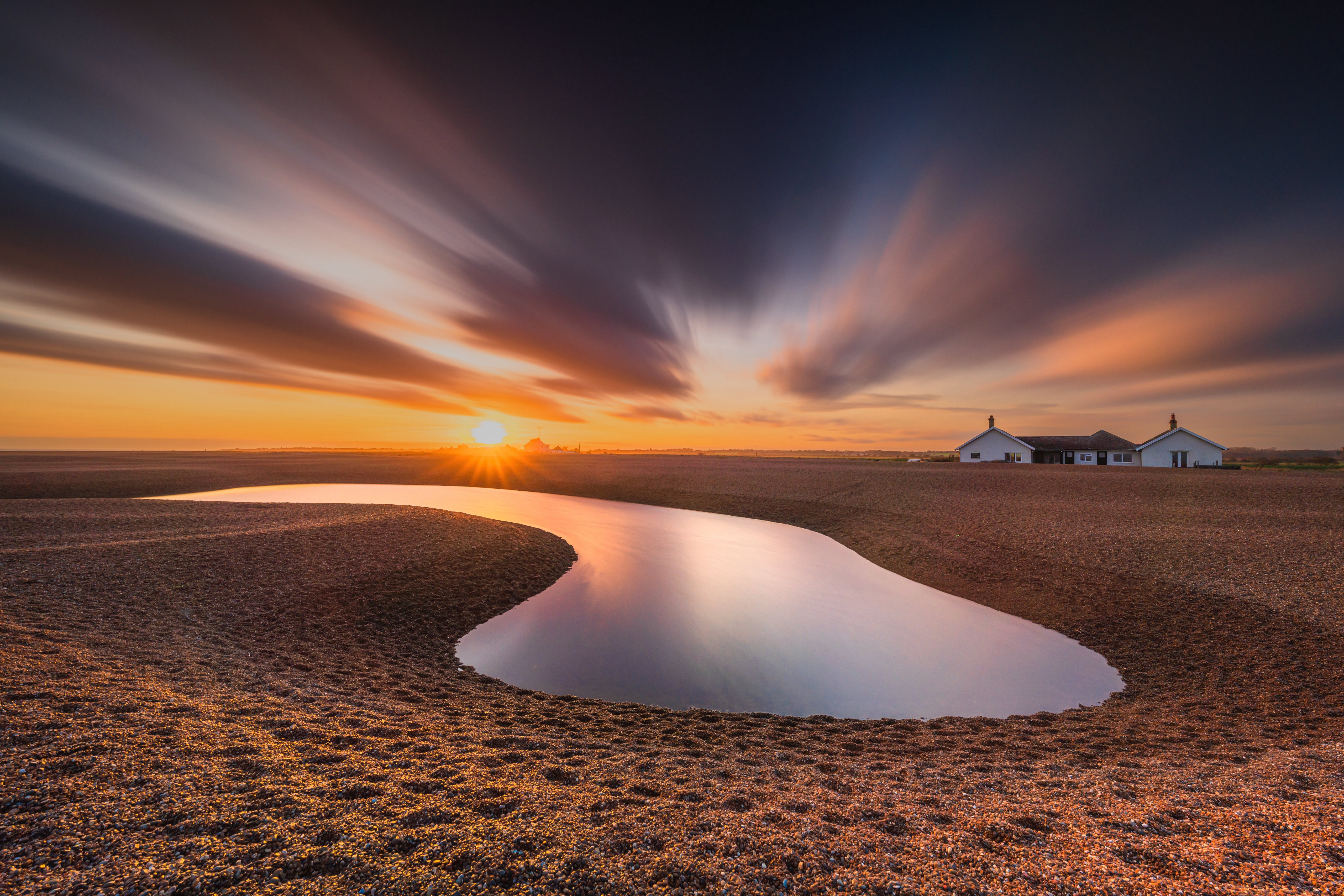 Sunrise over a pebble beach with a pond and houses HD Wallpaper