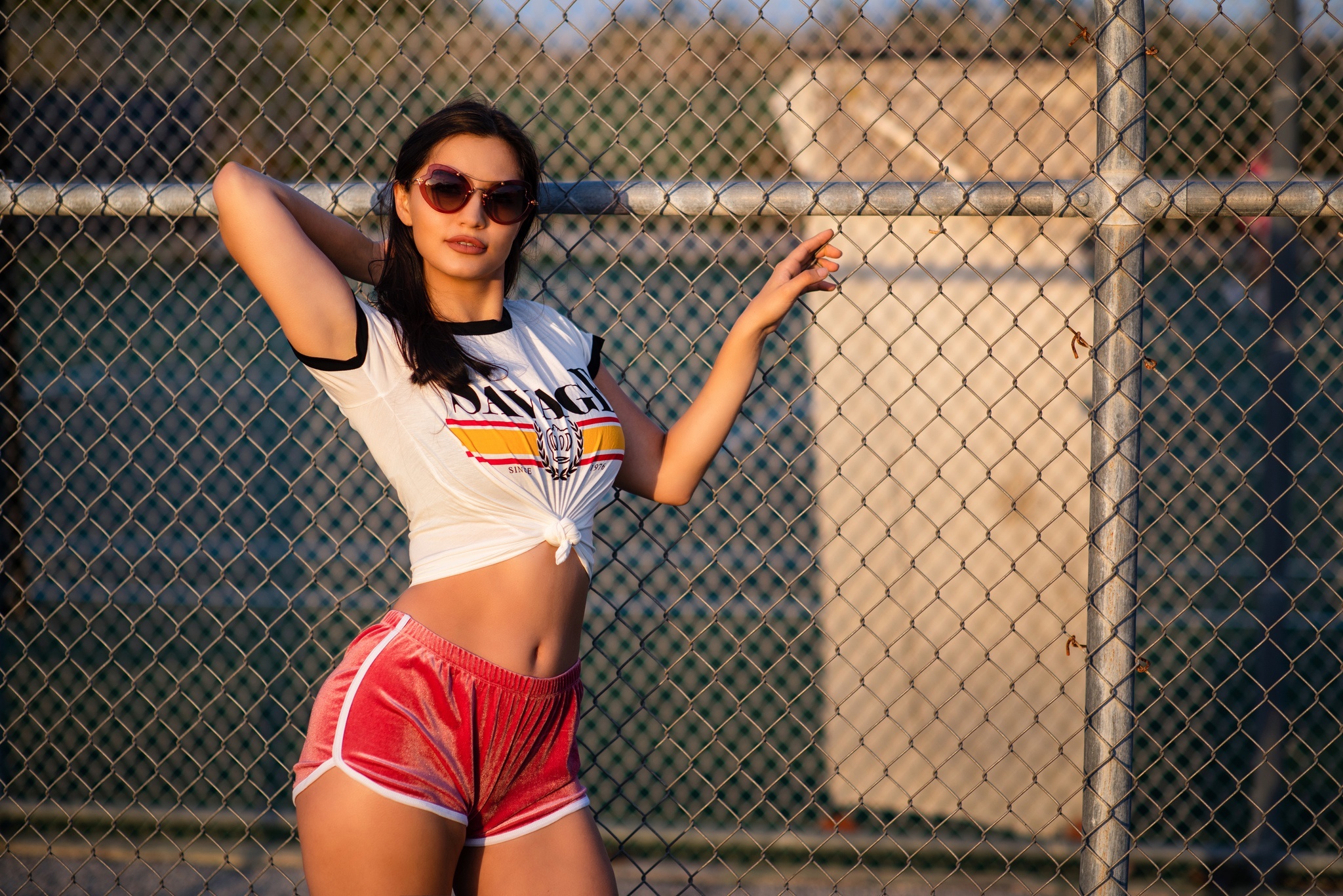 Woman in T-shirt and shorts posing by fence HD Wallpaper
