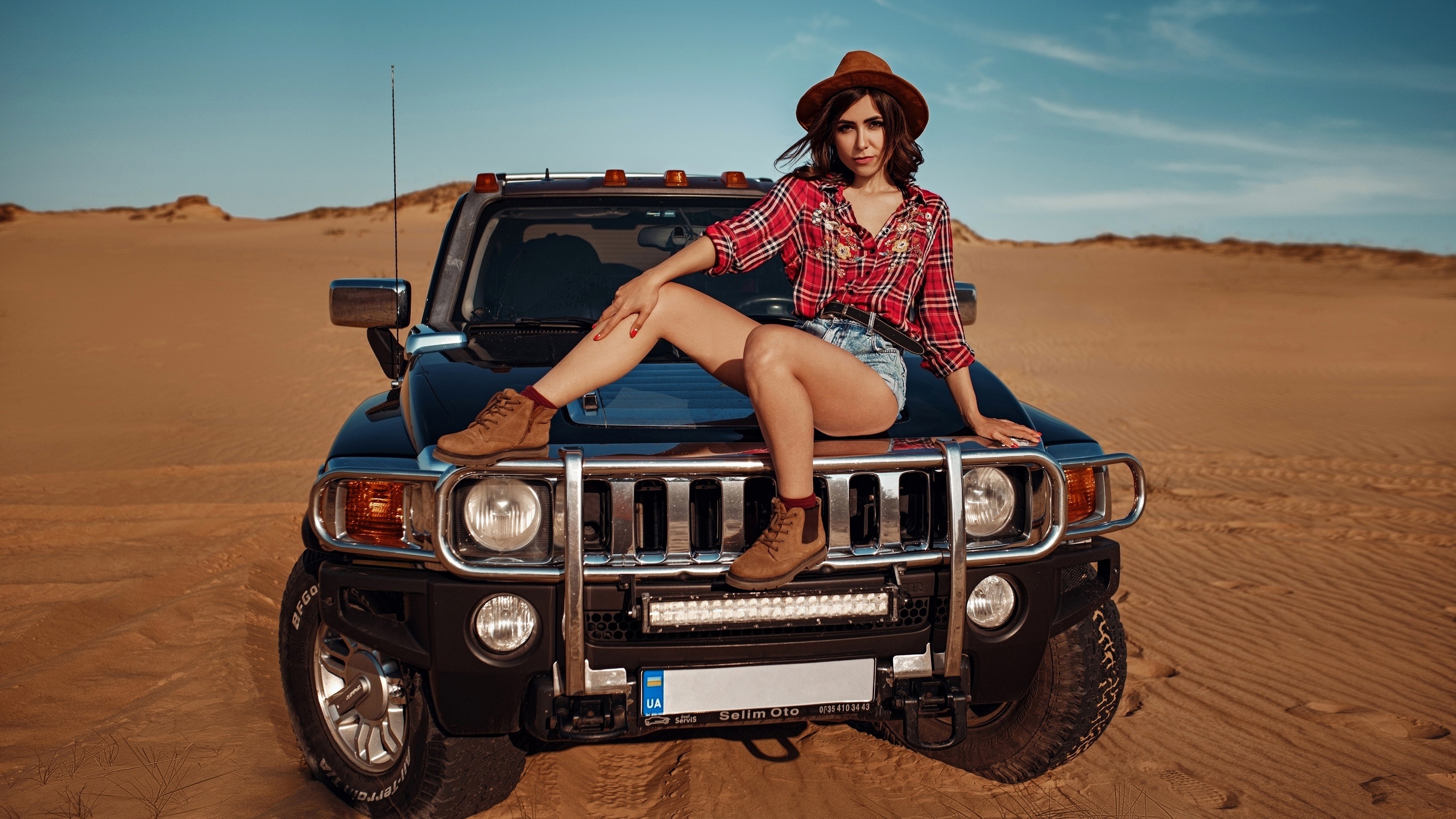 Woman in hat and plaid shirt sitting on a Hummer in the desert HD Wallpaper