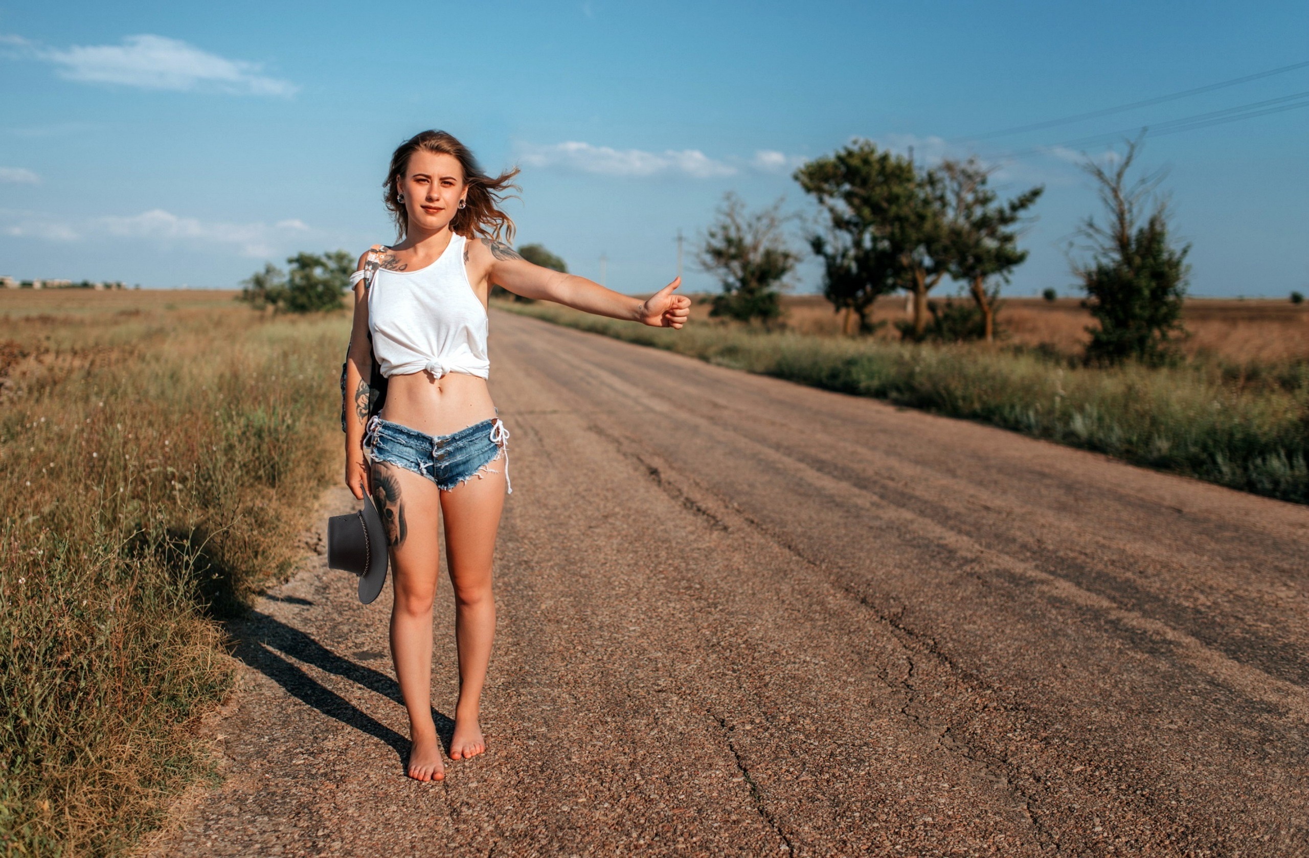 Woman hitch-hiking on a rural road with a hat HD Wallpaper