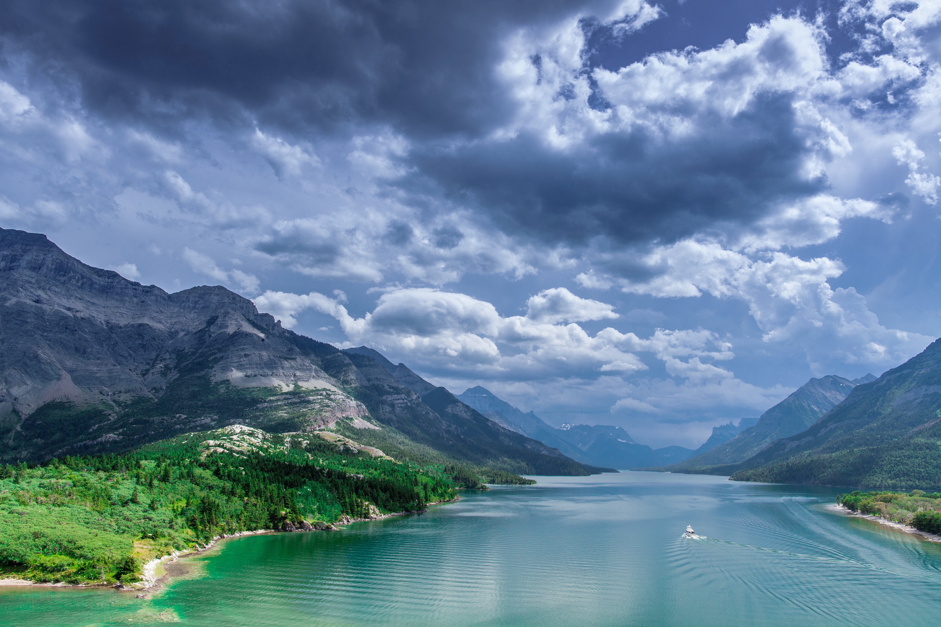 Boat on a lake with mountains and clouds in Waterton Lakes National Park HD Wallpaper