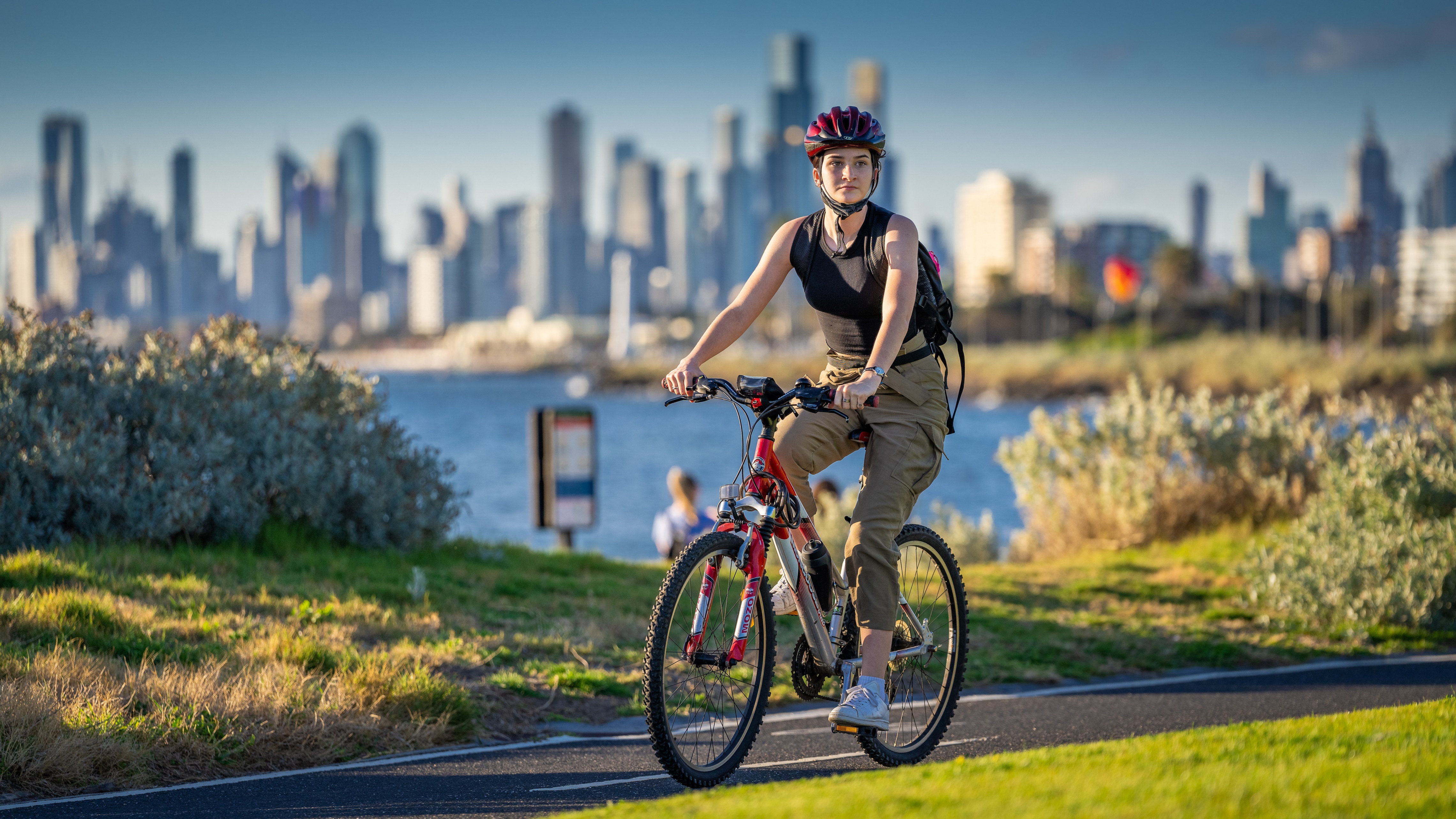 Woman riding a bicycle with a city skyline in the background HD Wallpaper