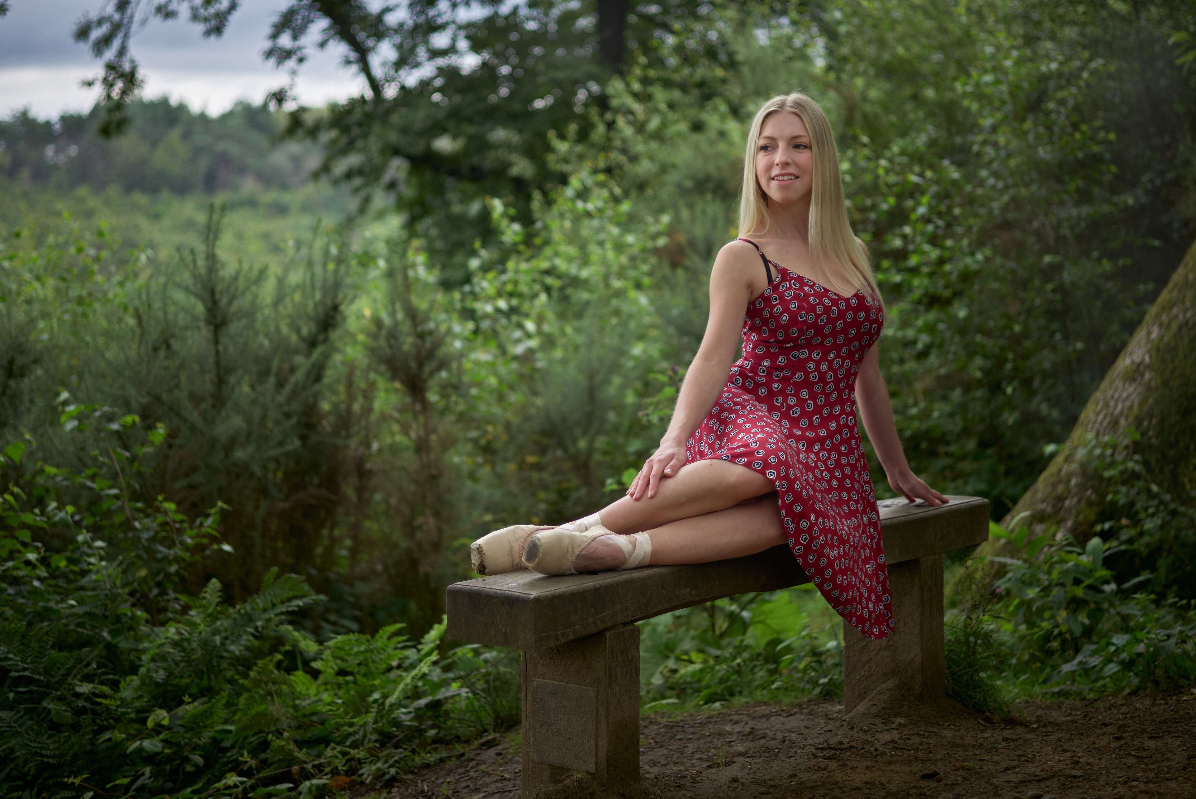 Blonde girl in red dress sitting on bench in forest HD Wallpaper