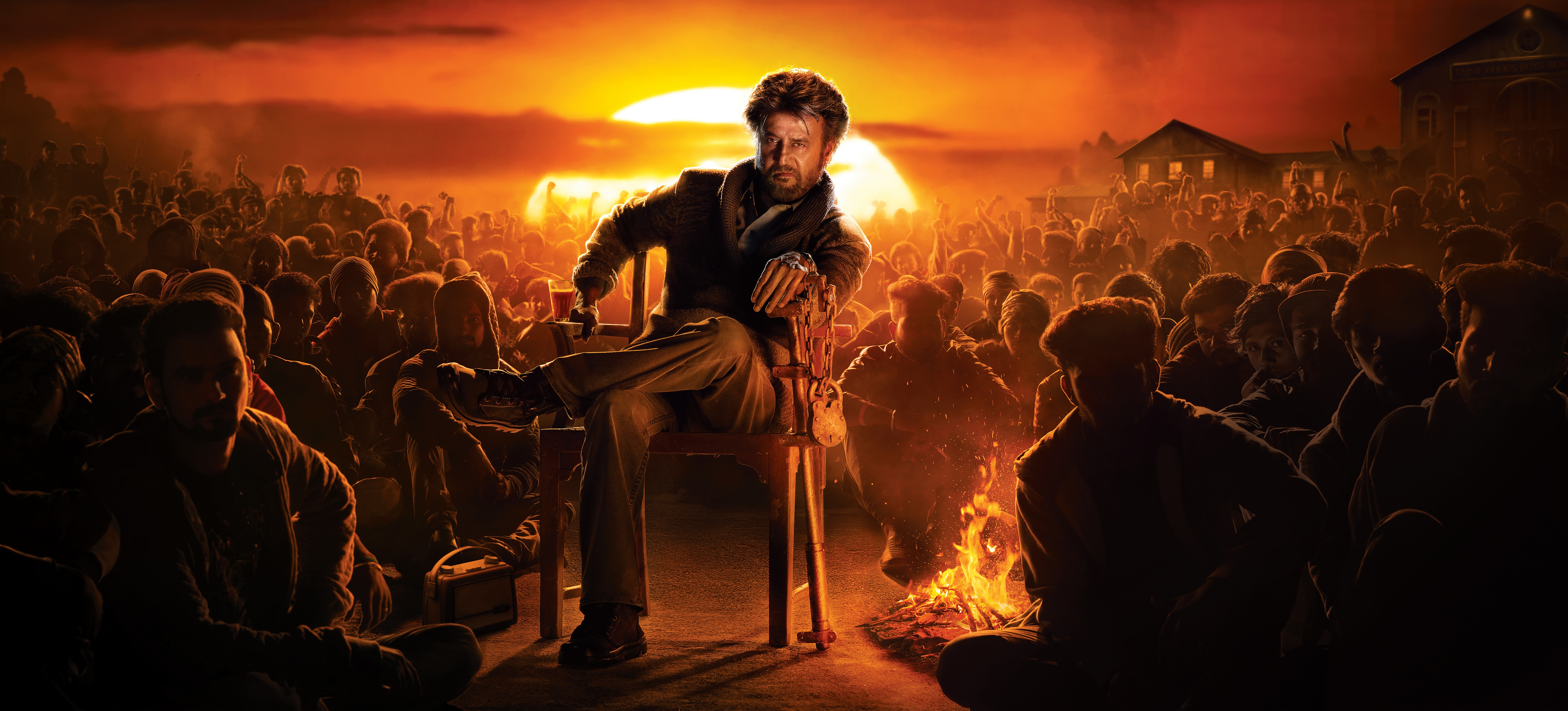 Rajinikanth sitting in front of a crowd at sunset HD Wallpaper