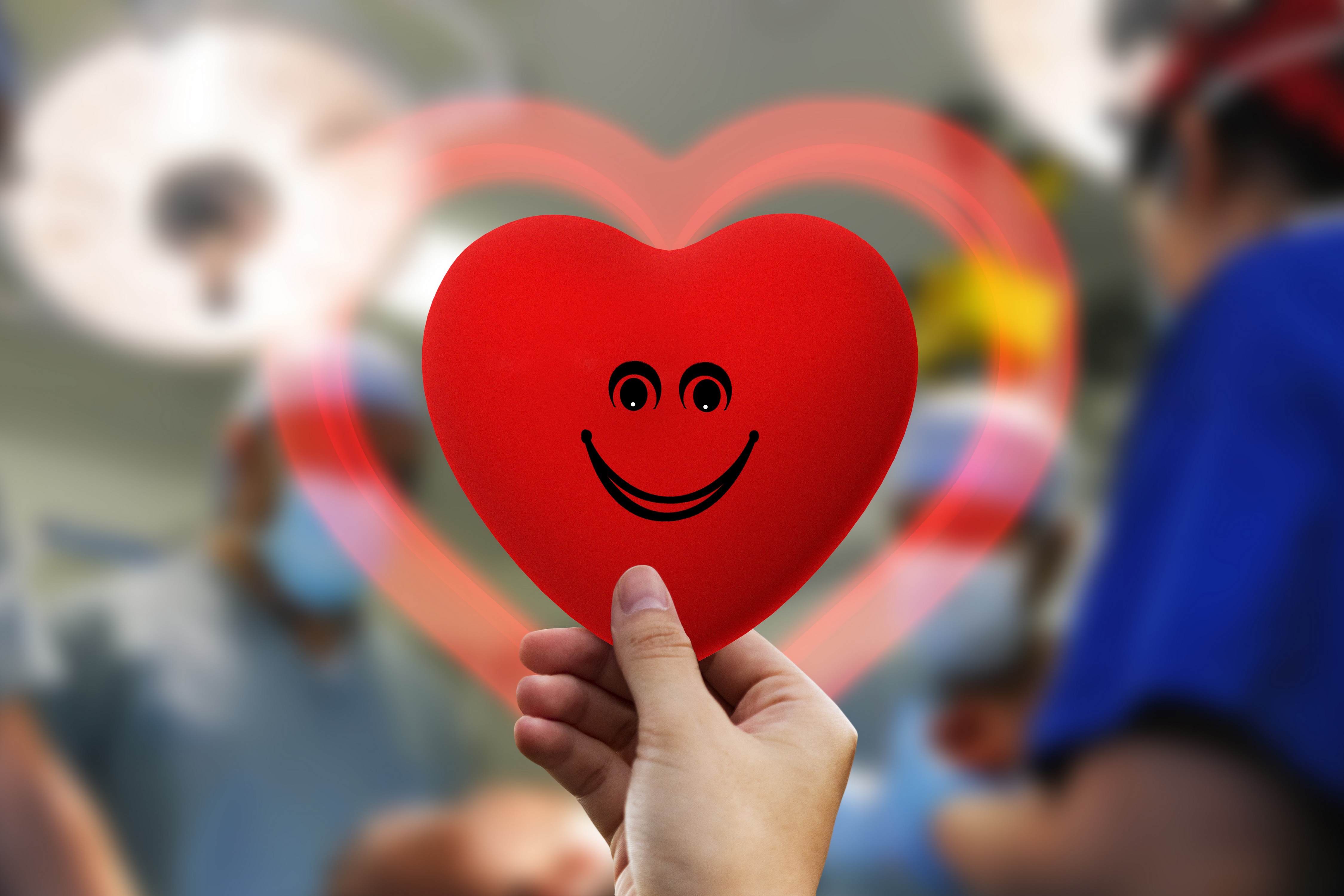 Hand holding a smiley heart in front of blurred medical staff HD Wallpaper