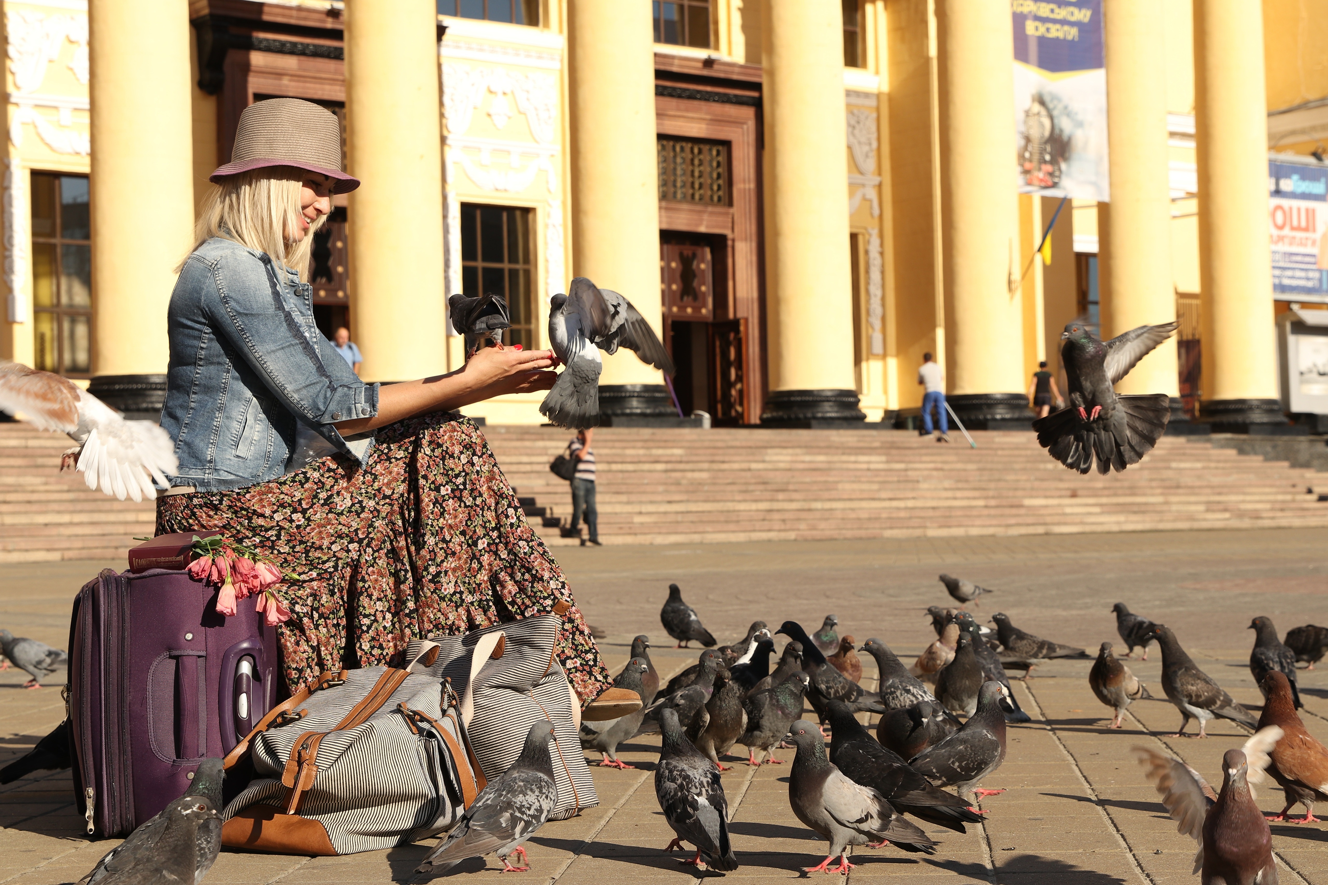 Blonde girl in hat feeding pigeons with luggage HD Wallpaper