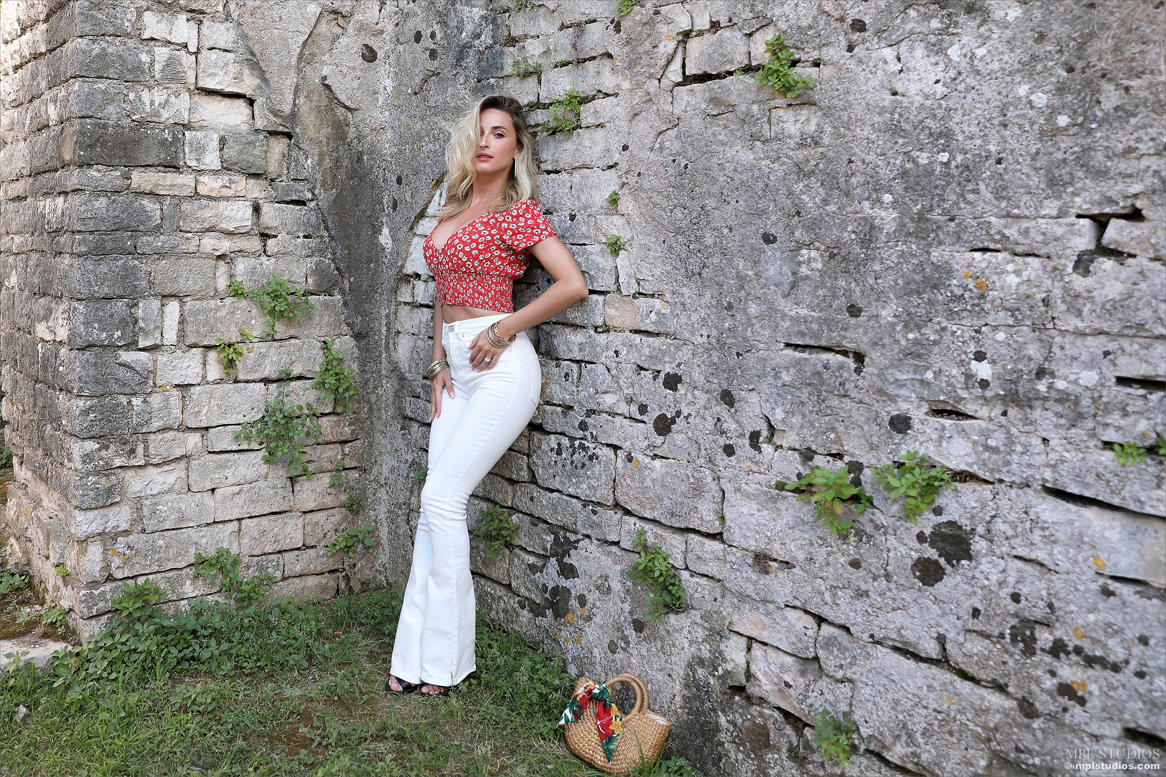 Cara Mell in red blouse and white jeans posing by stone wall HD Wallpaper