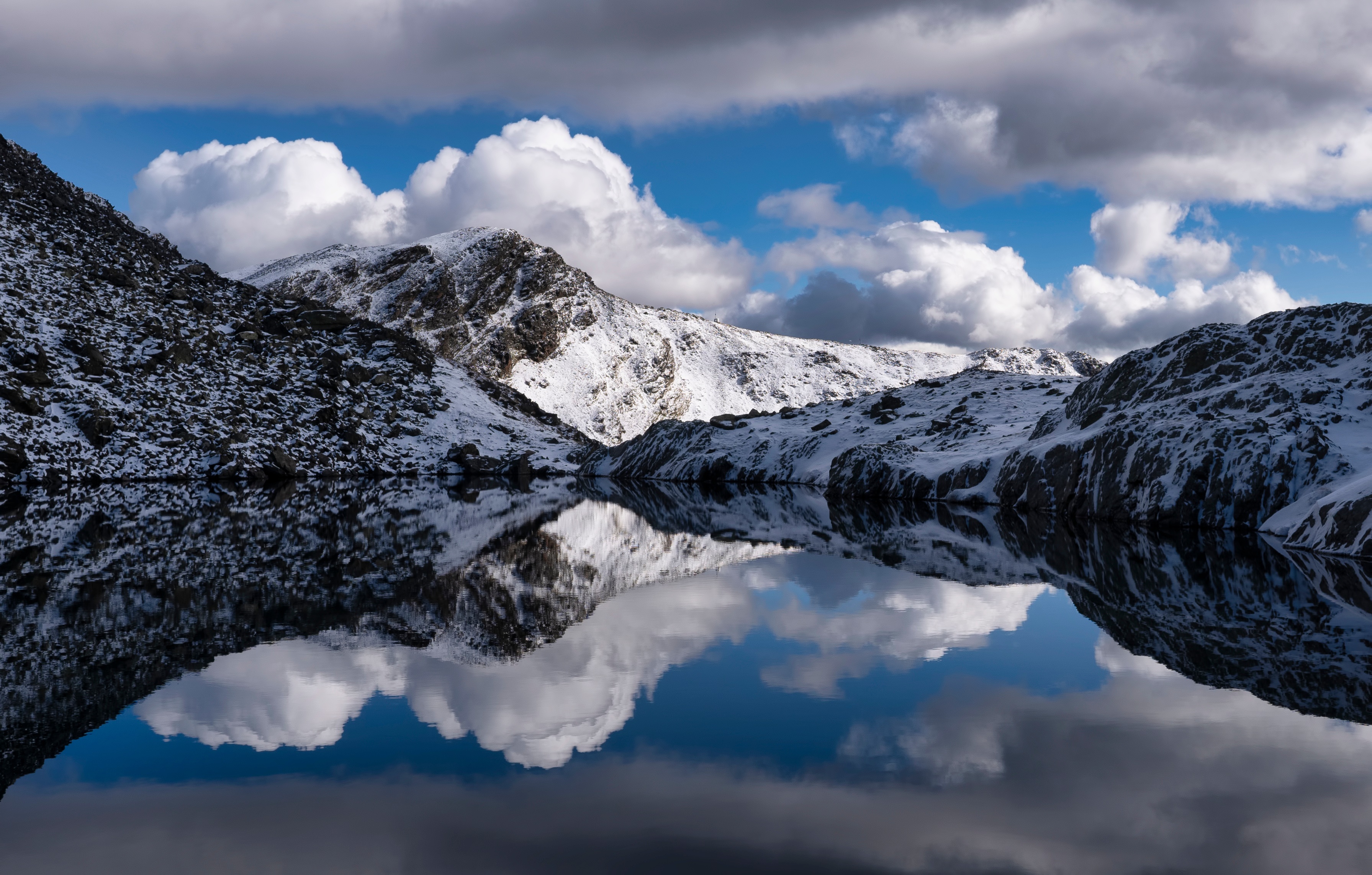 Snow-covered mountains reflected in a lake under cloudy sky HD Wallpaper