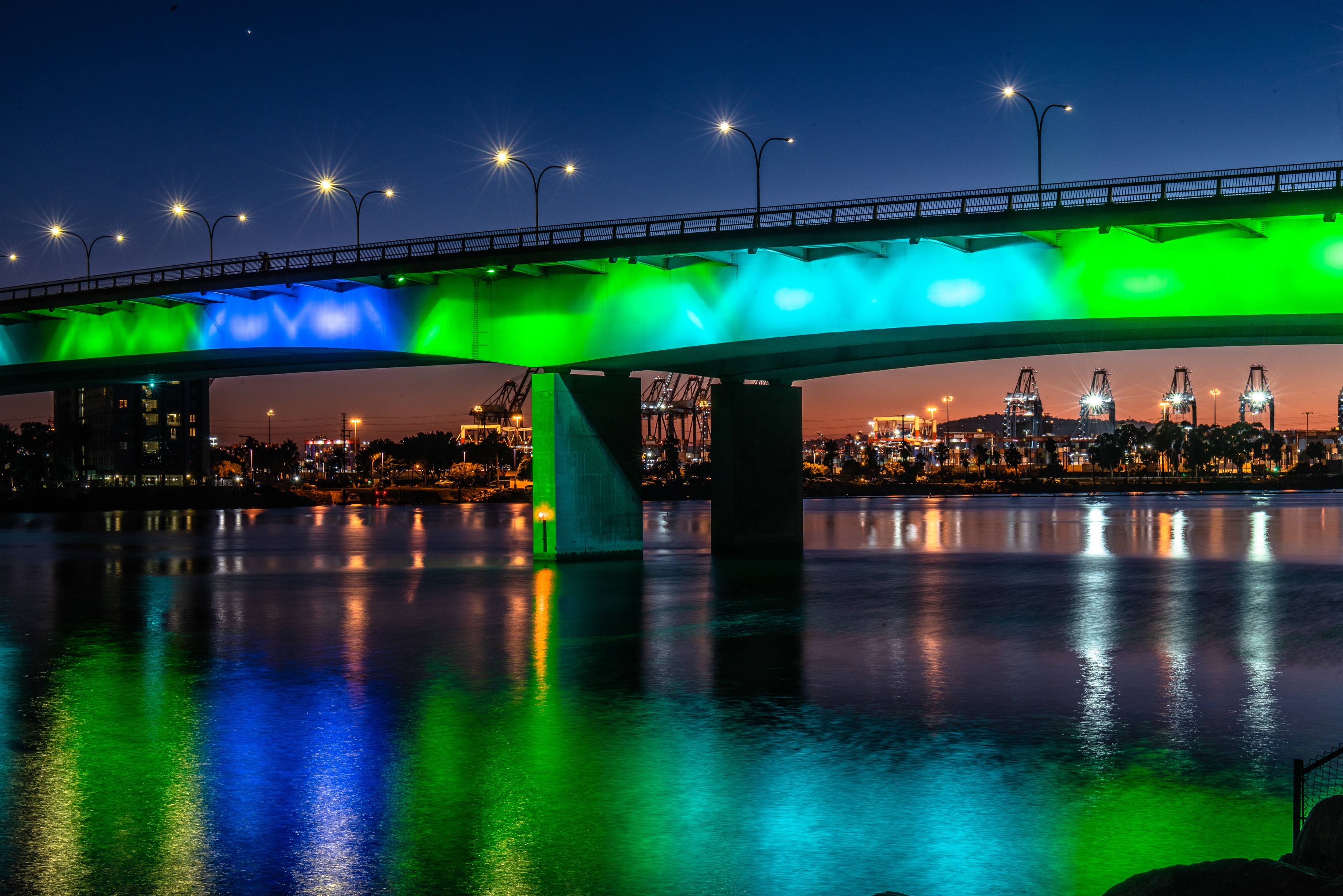Queensway Bridge illuminated with green and blue lights over water at night HD Wallpaper