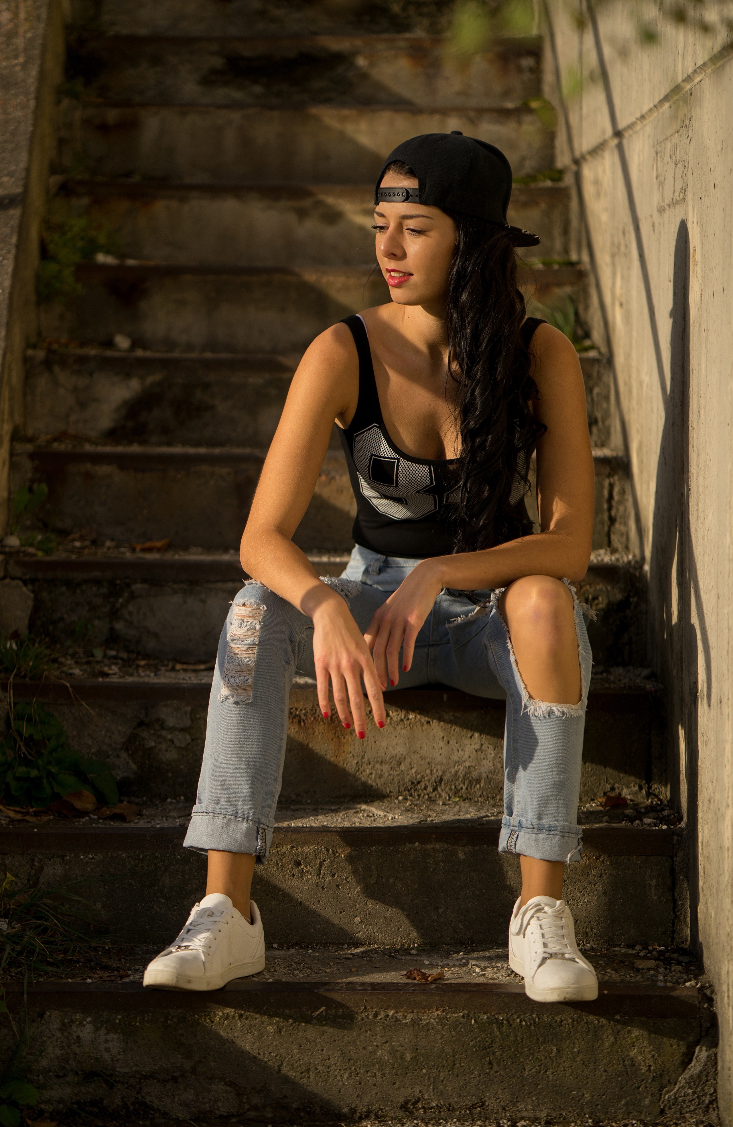 Brunette girl wearing a baseball cap and ripped jeans sitting on stairs HD Phone Wallpaper