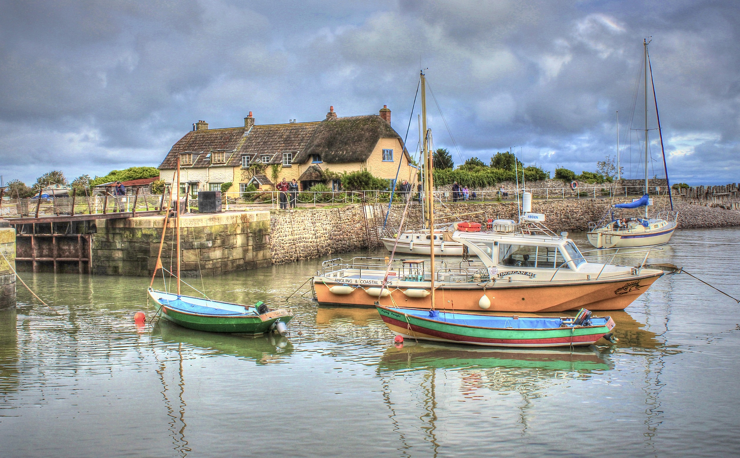 Boats docked in a harbor with thatched-roof houses HD Wallpaper
