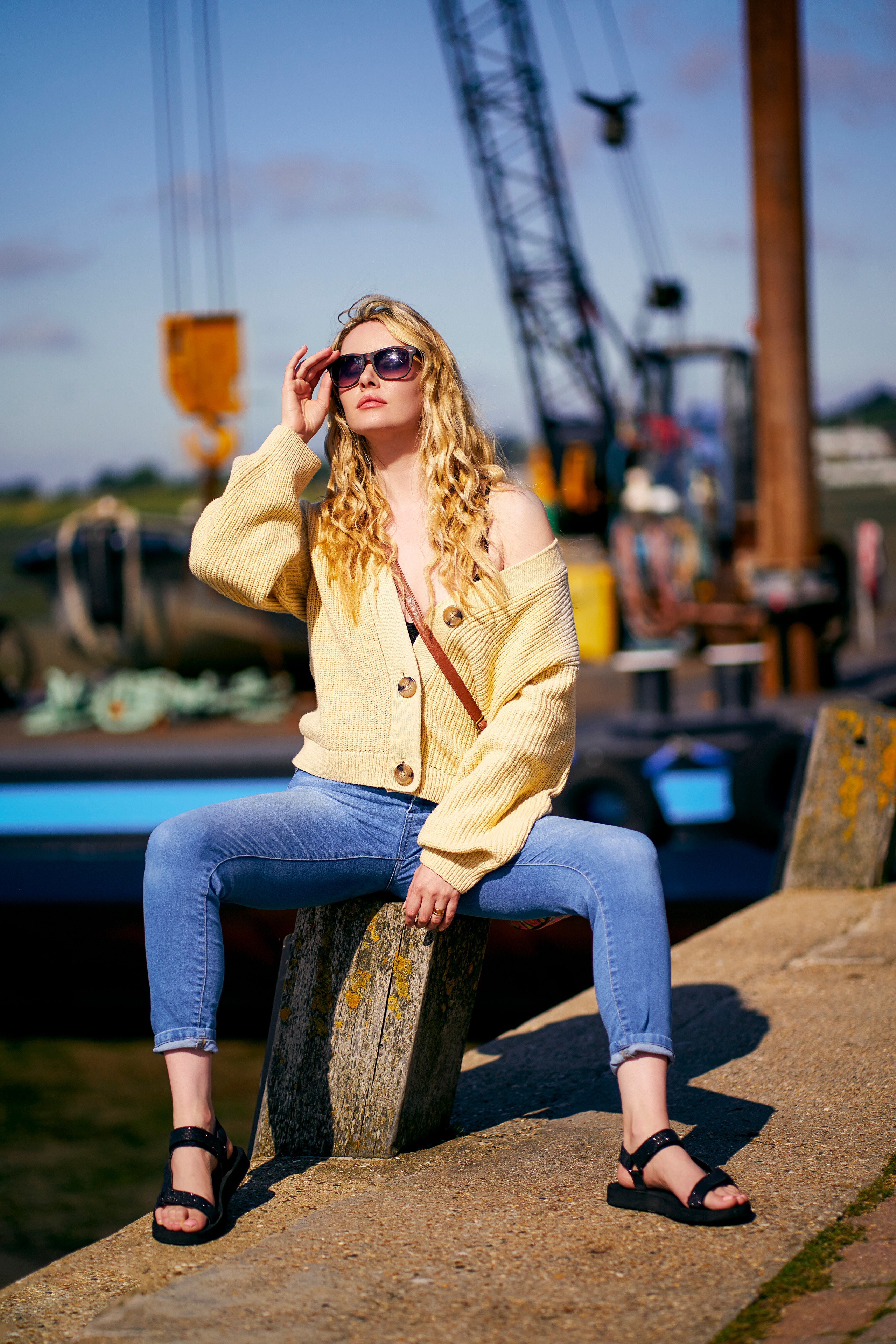 Blonde woman wearing sunglasses and yellow cardigan sitting outdoors HD Phone Wallpaper