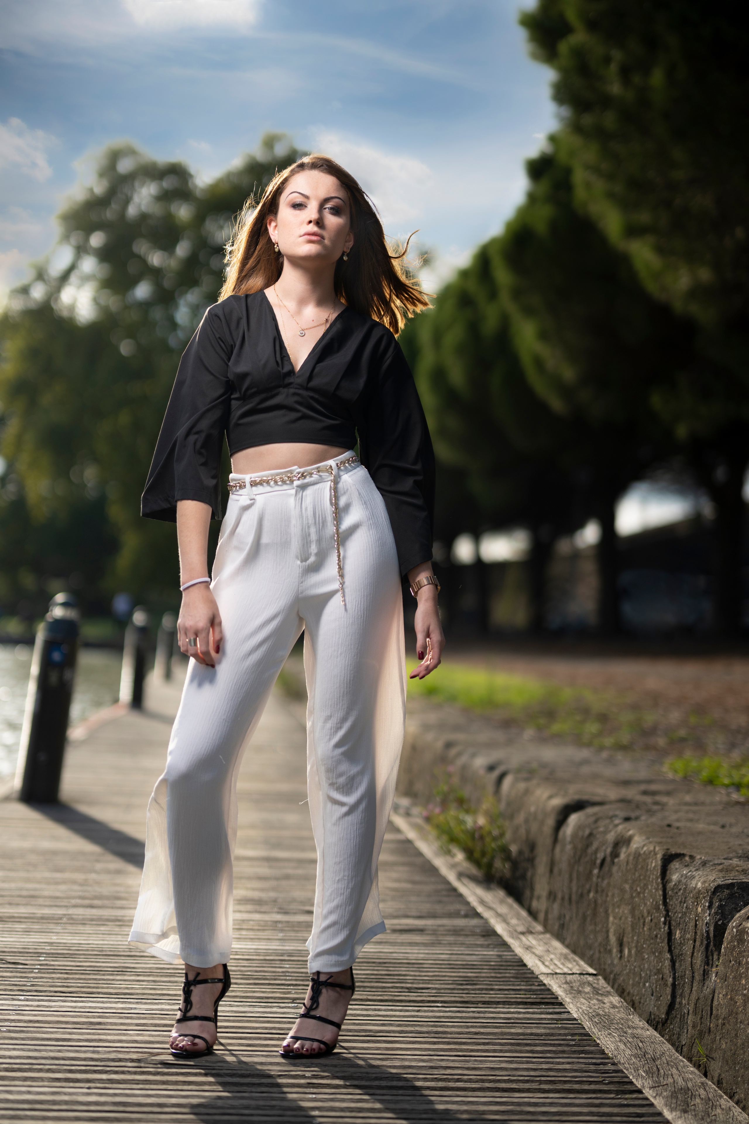 Woman in black blouse and white trousers posing outdoors HD Phone Wallpaper