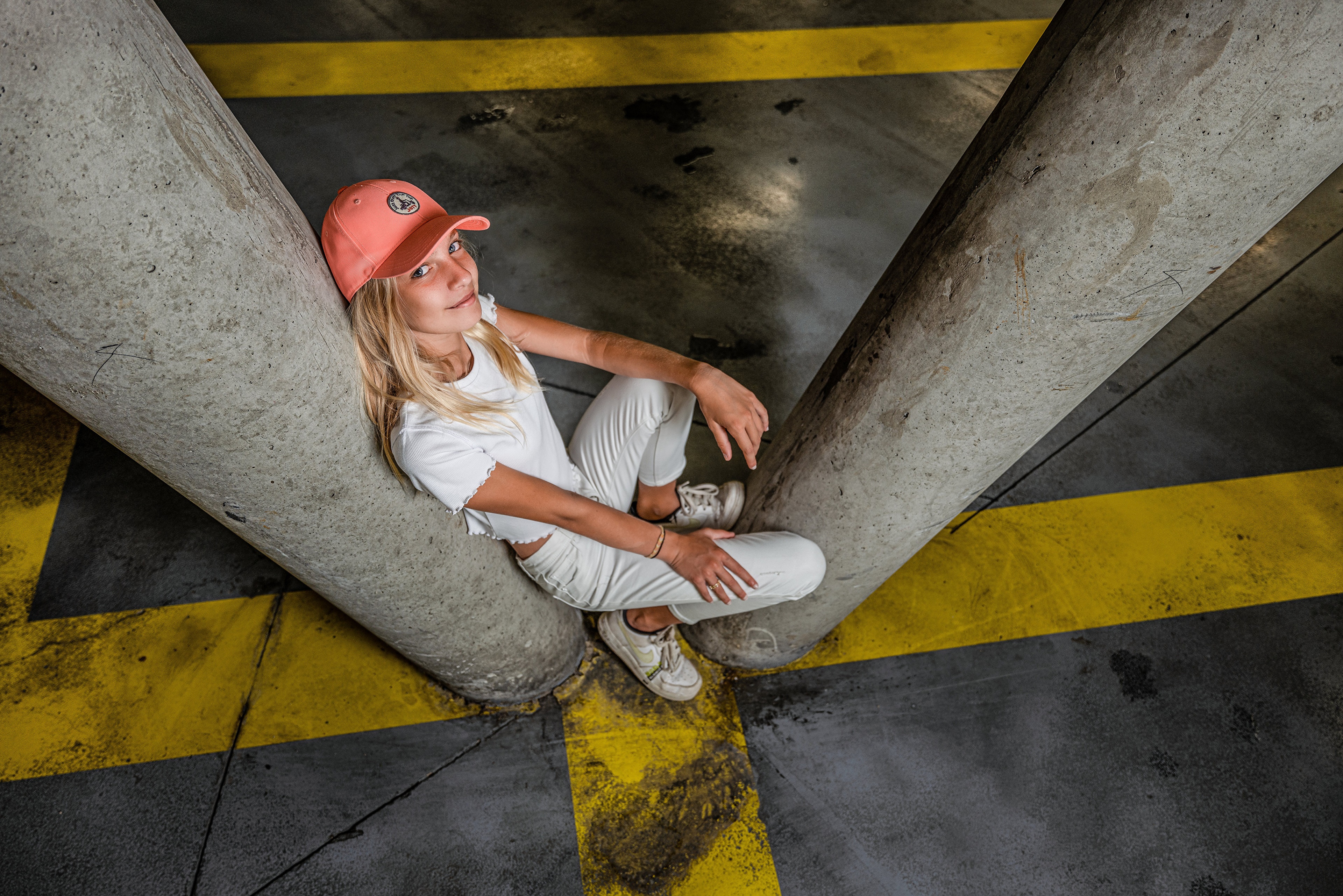 Blonde girl in baseball cap sitting between concrete pillars HD Wallpaper