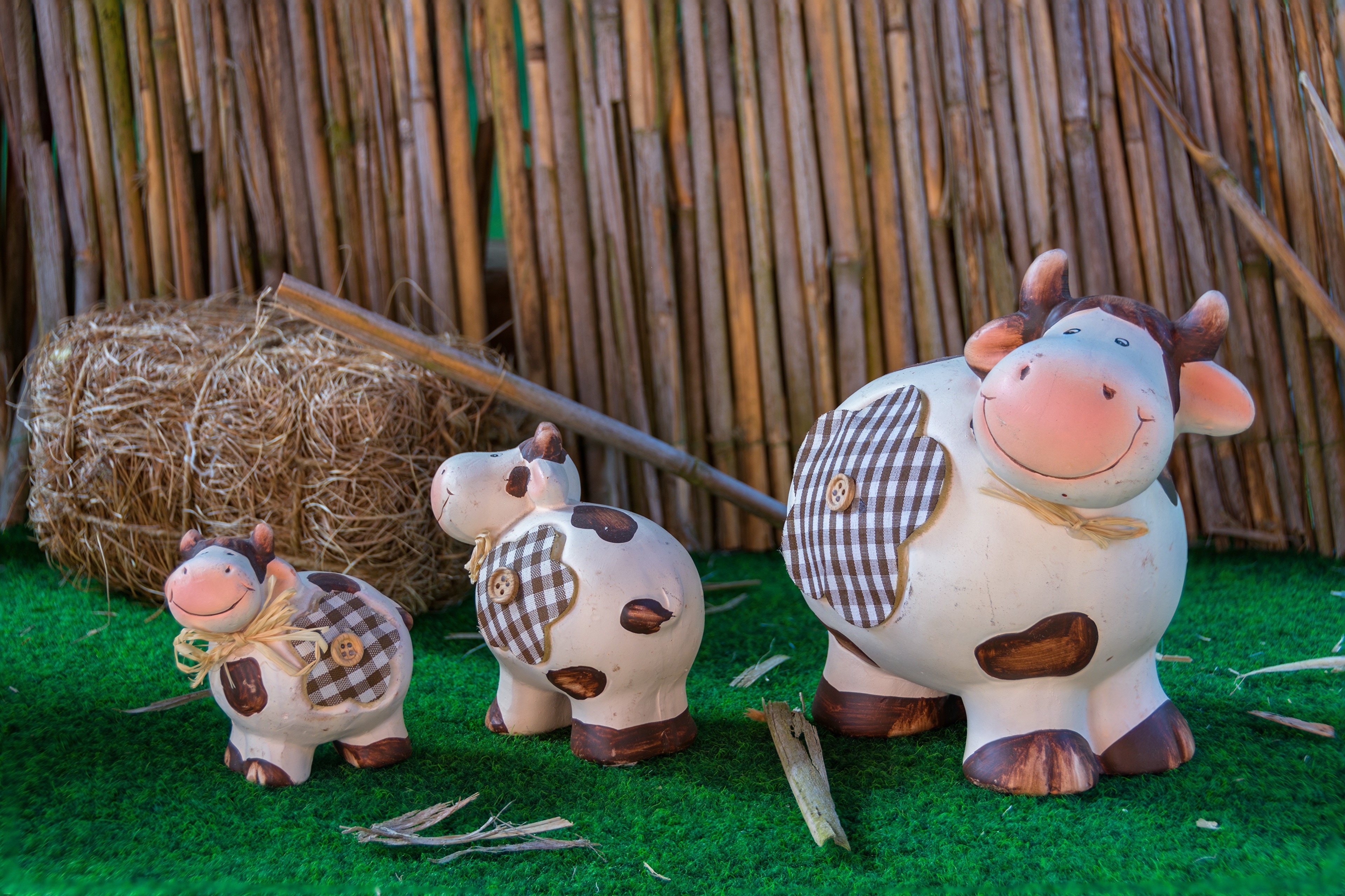 Three toy cows on grass with hay and bamboo background HD Wallpaper