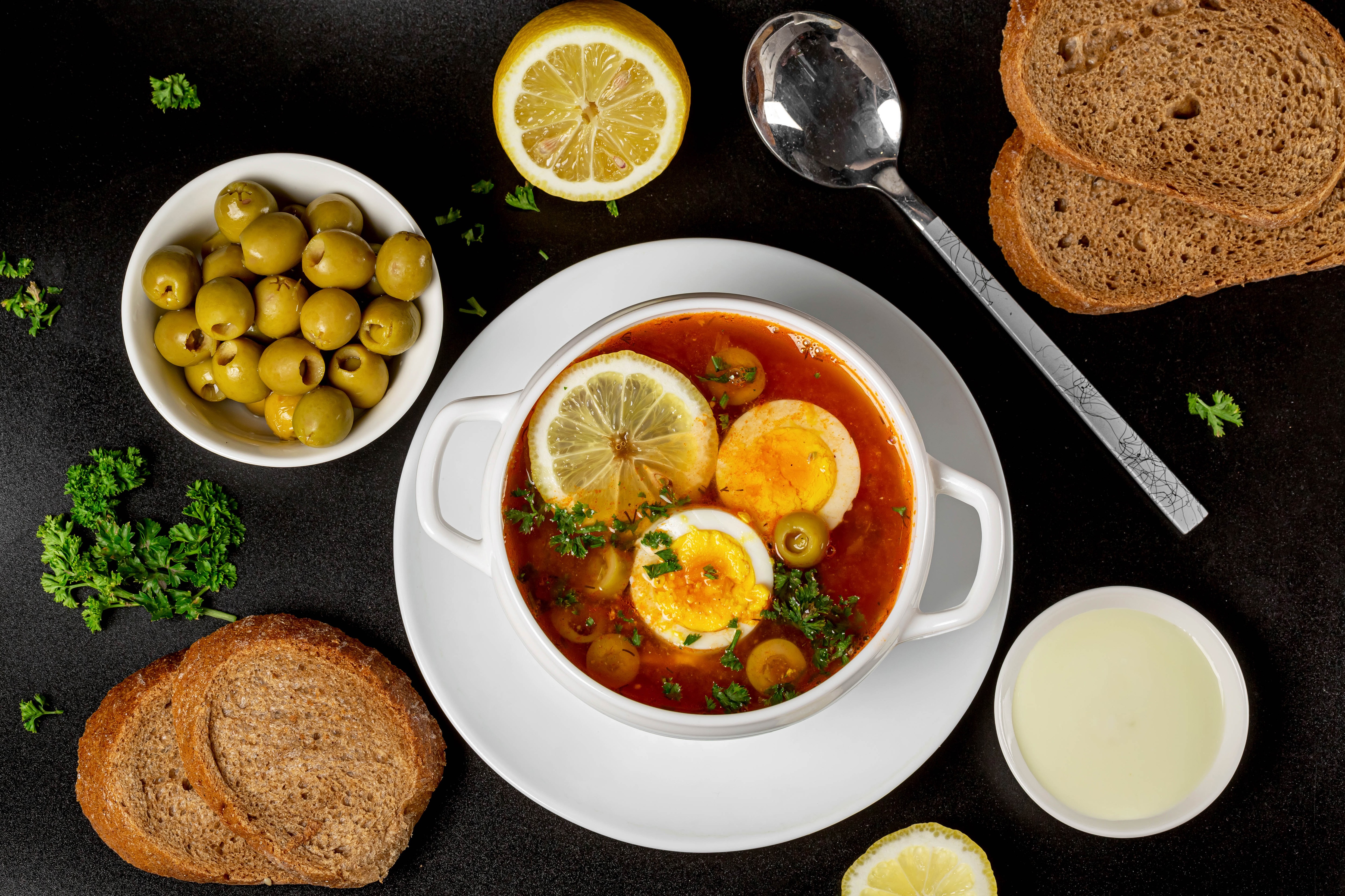 Soup with eggs, olives, lemon, bread, and spoon HD Wallpaper