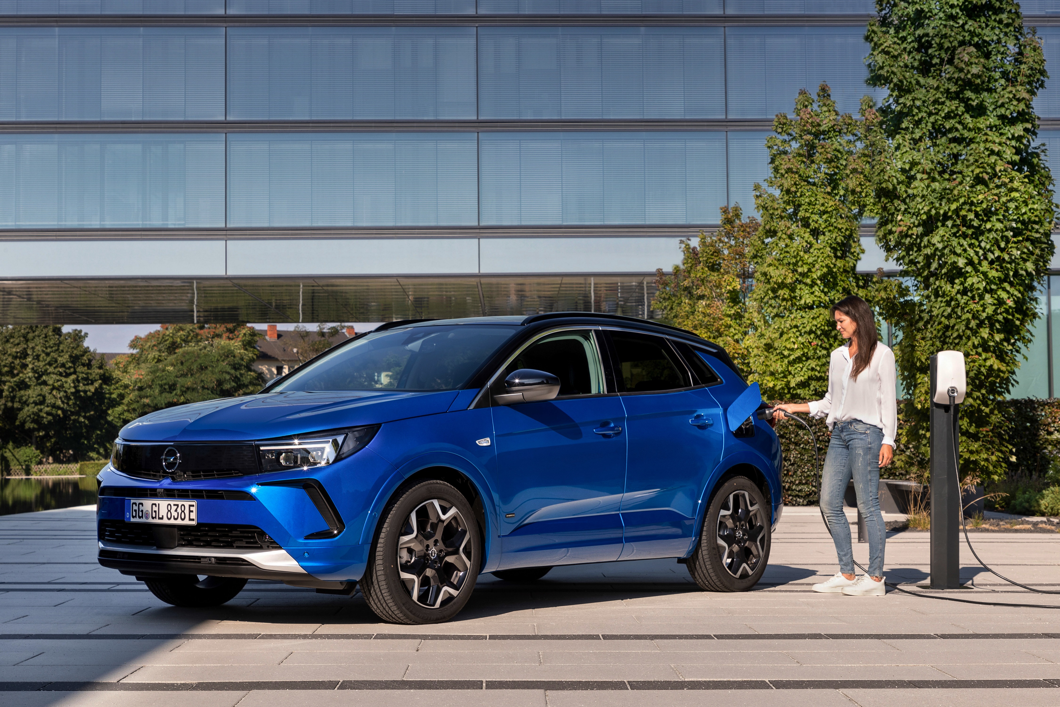 Opel Grandland Hybrid4 charging in front of a modern building HD Wallpaper