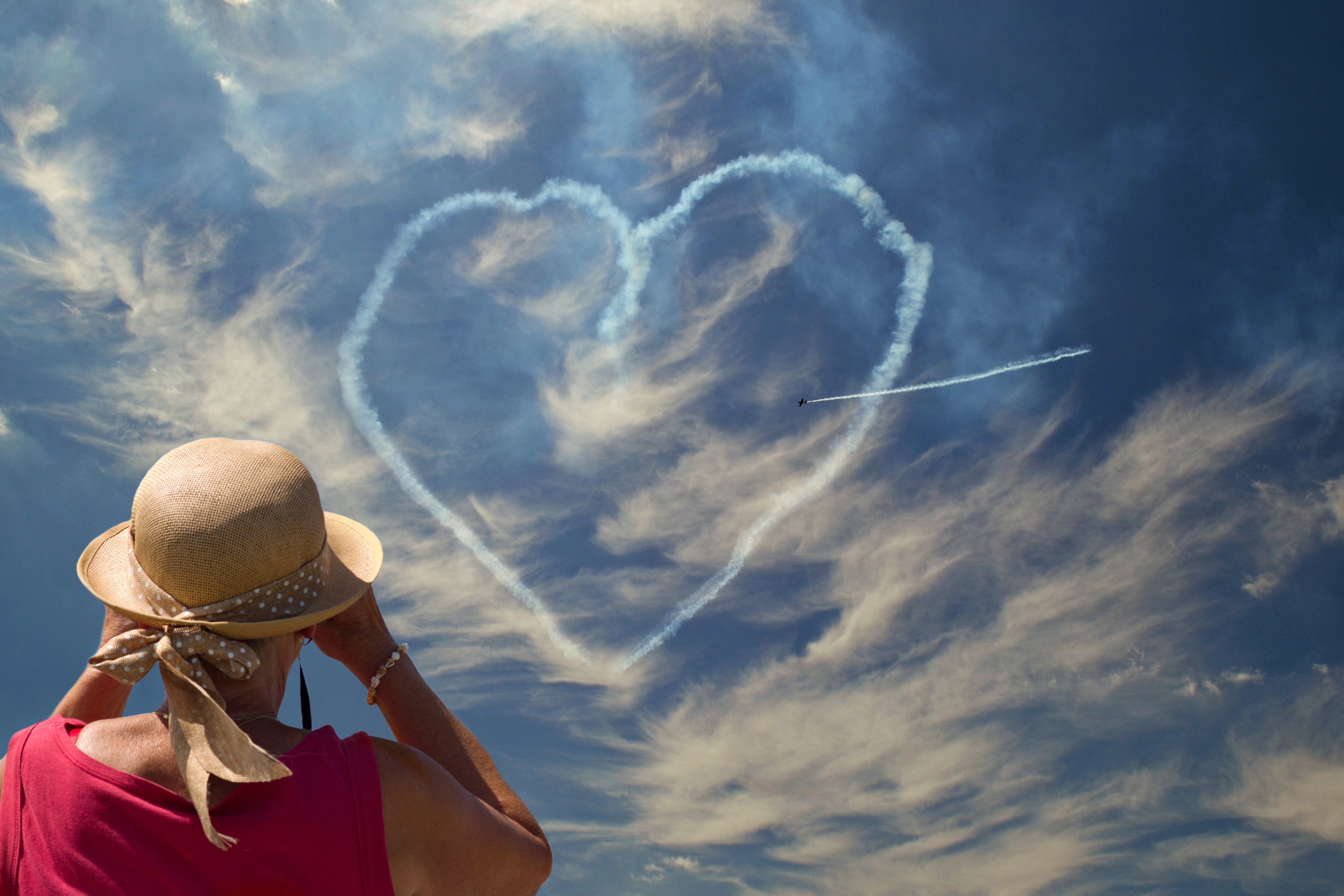 Woman watches plane draw heart in sky HD Wallpaper