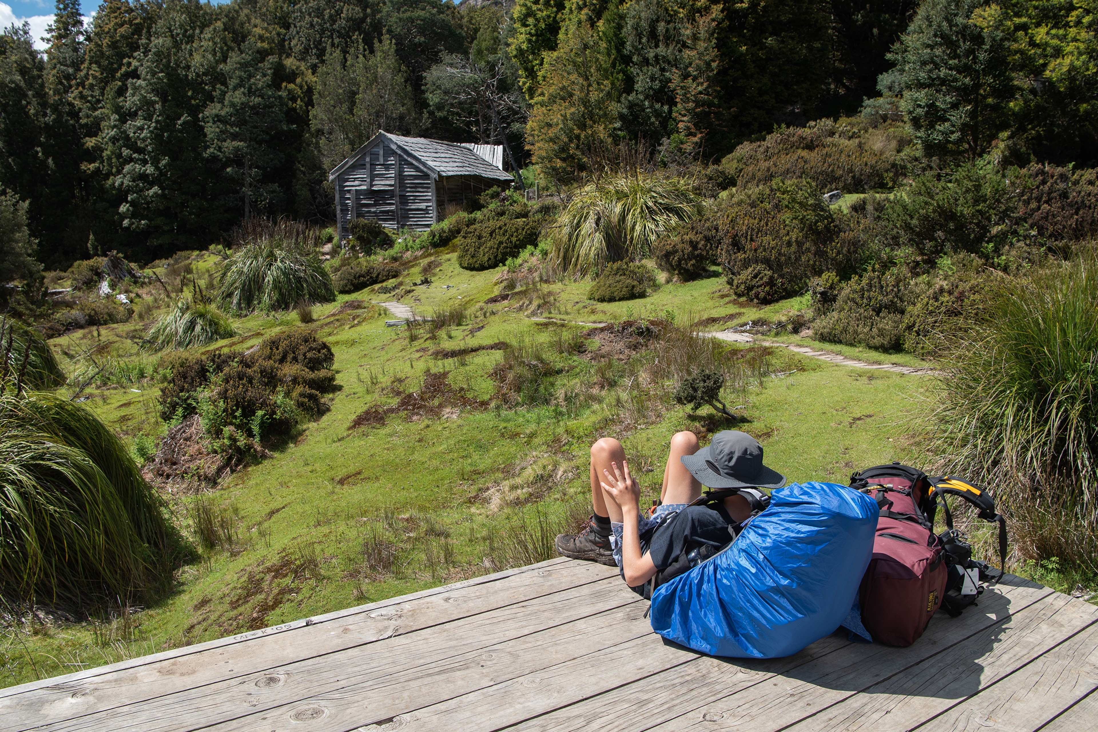 Backpacker resting near a rustic cabin in Tasmania, Australia HD Wallpaper