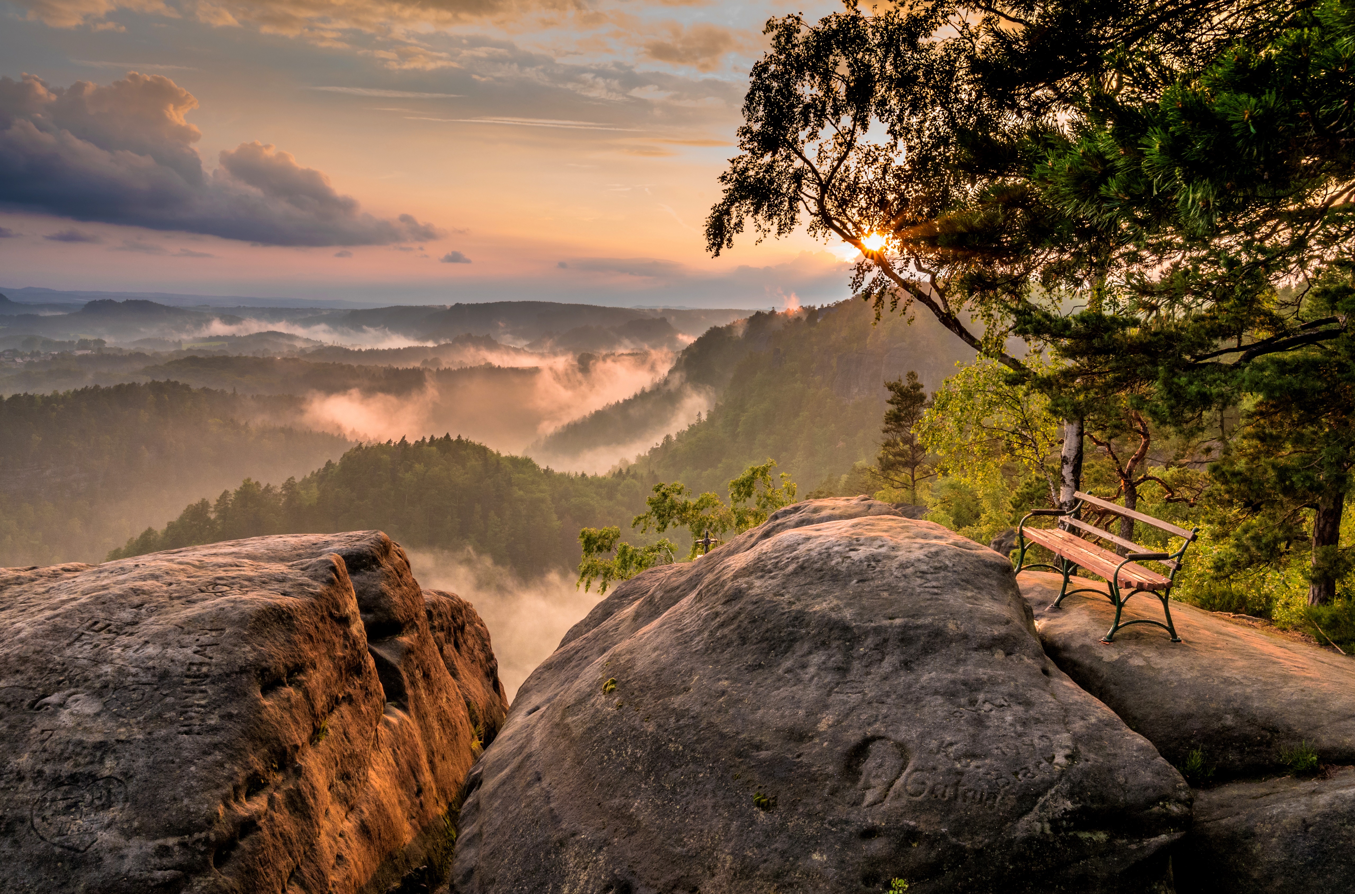 Bench on a rocky outcrop overlooking a misty valley at sunset in Saxony, Germany HD Wallpaper