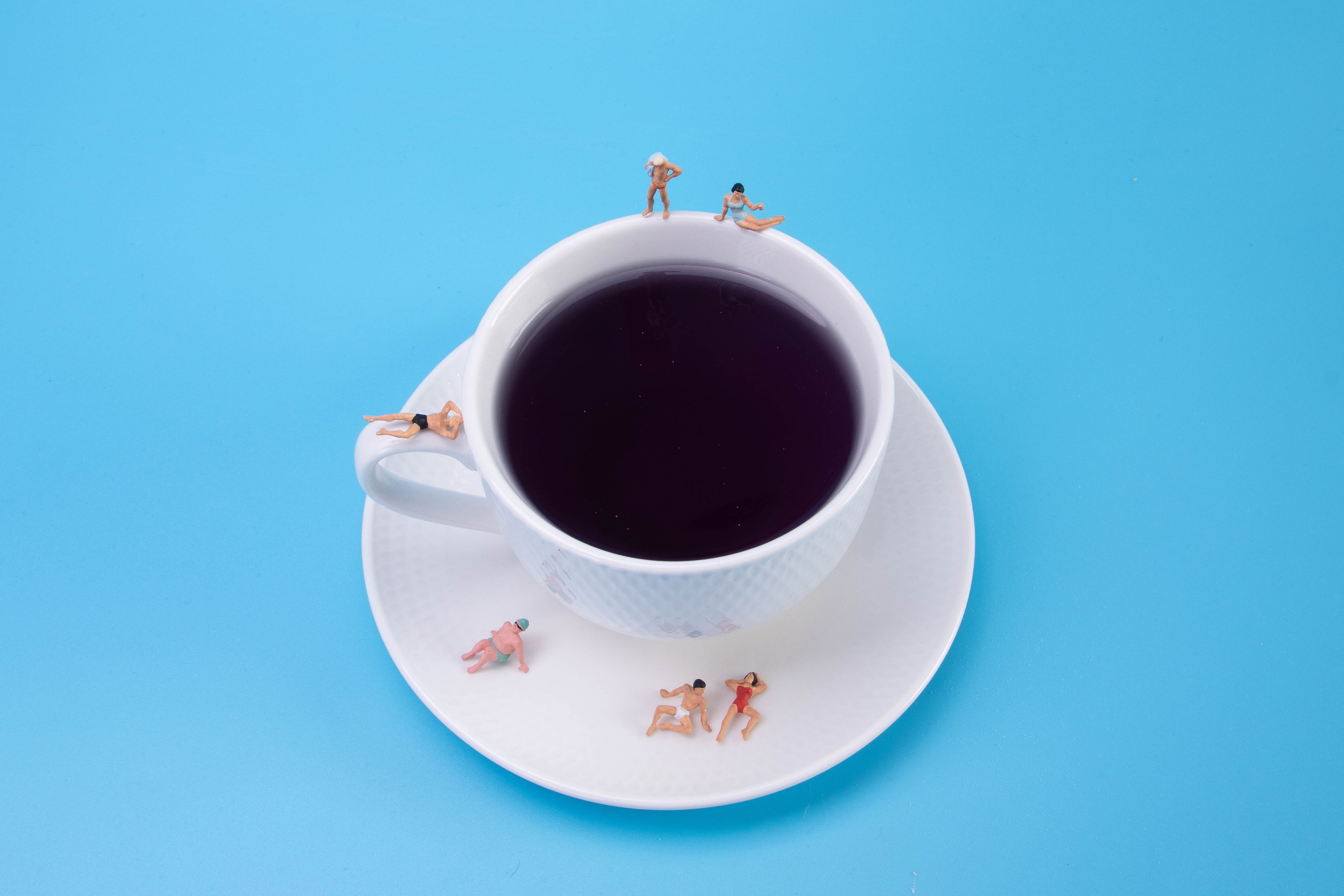 Miniature people sunbathing on a coffee cup and saucer HD Wallpaper