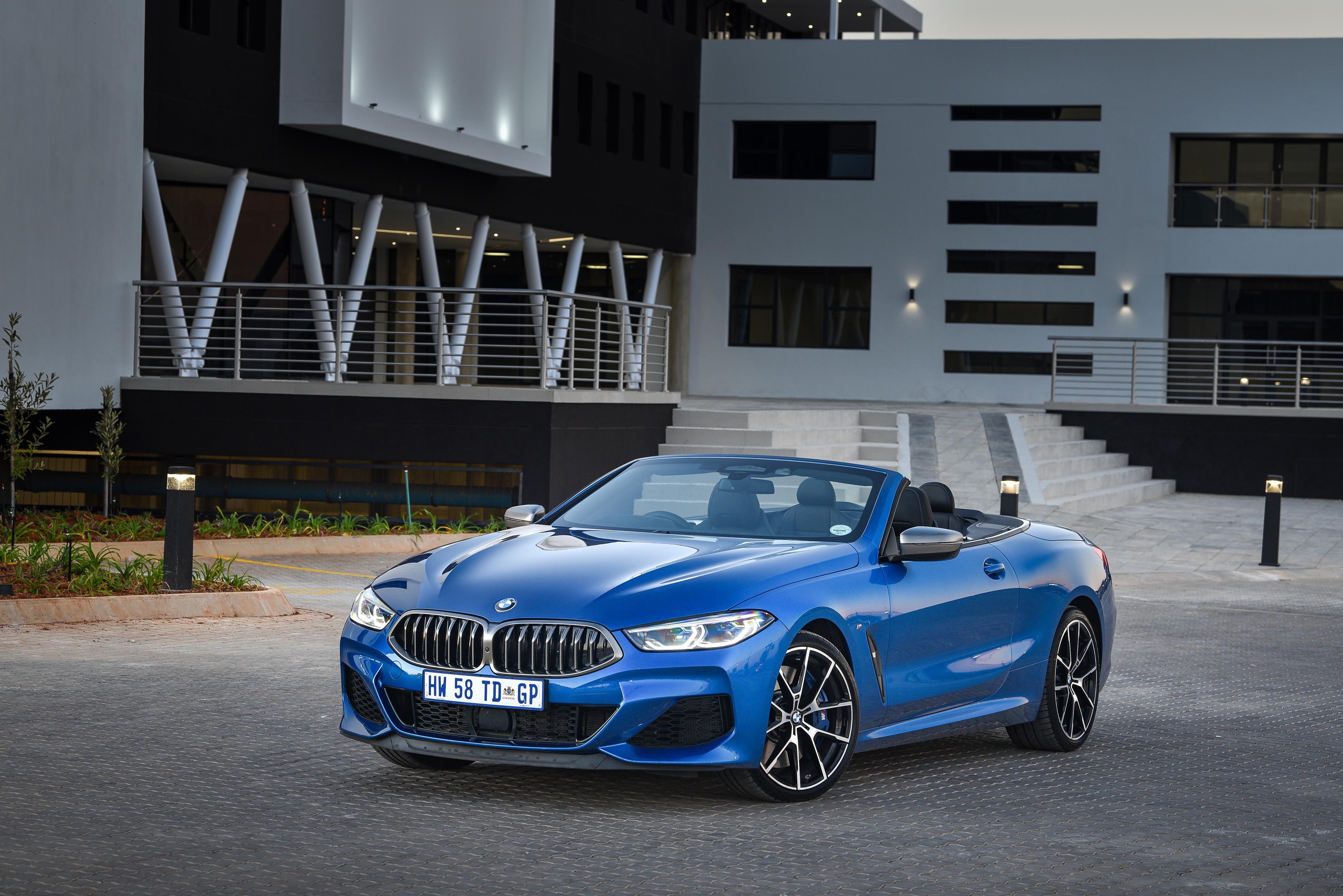 Blue BMW M850i xDrive Convertible parked in front of a modern building HD Wallpaper